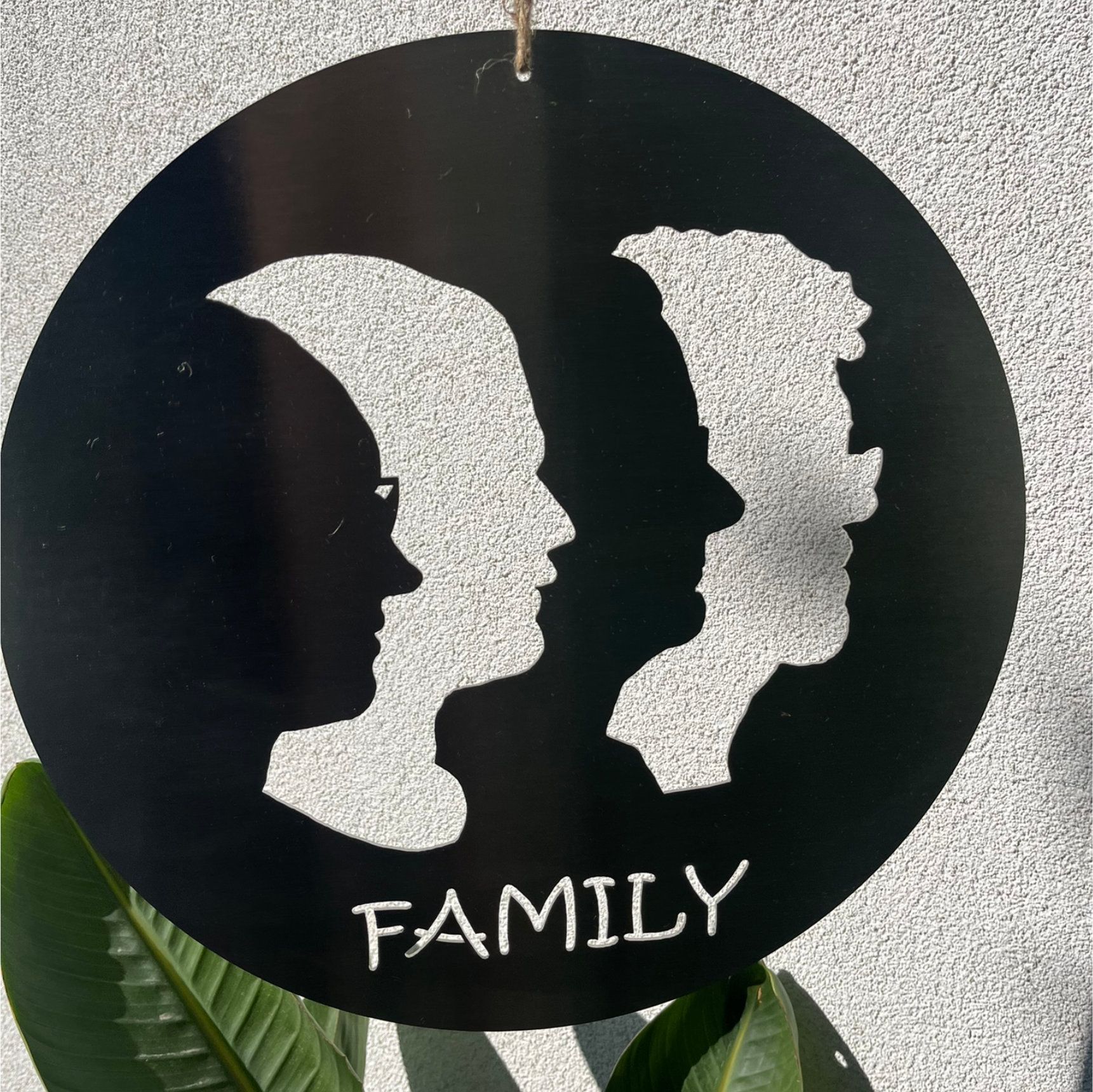 Schwarze Metall-Familiensilhouette mit dem Schriftzug „FAMILY“, runde Form, an einer Schnur hängend.
