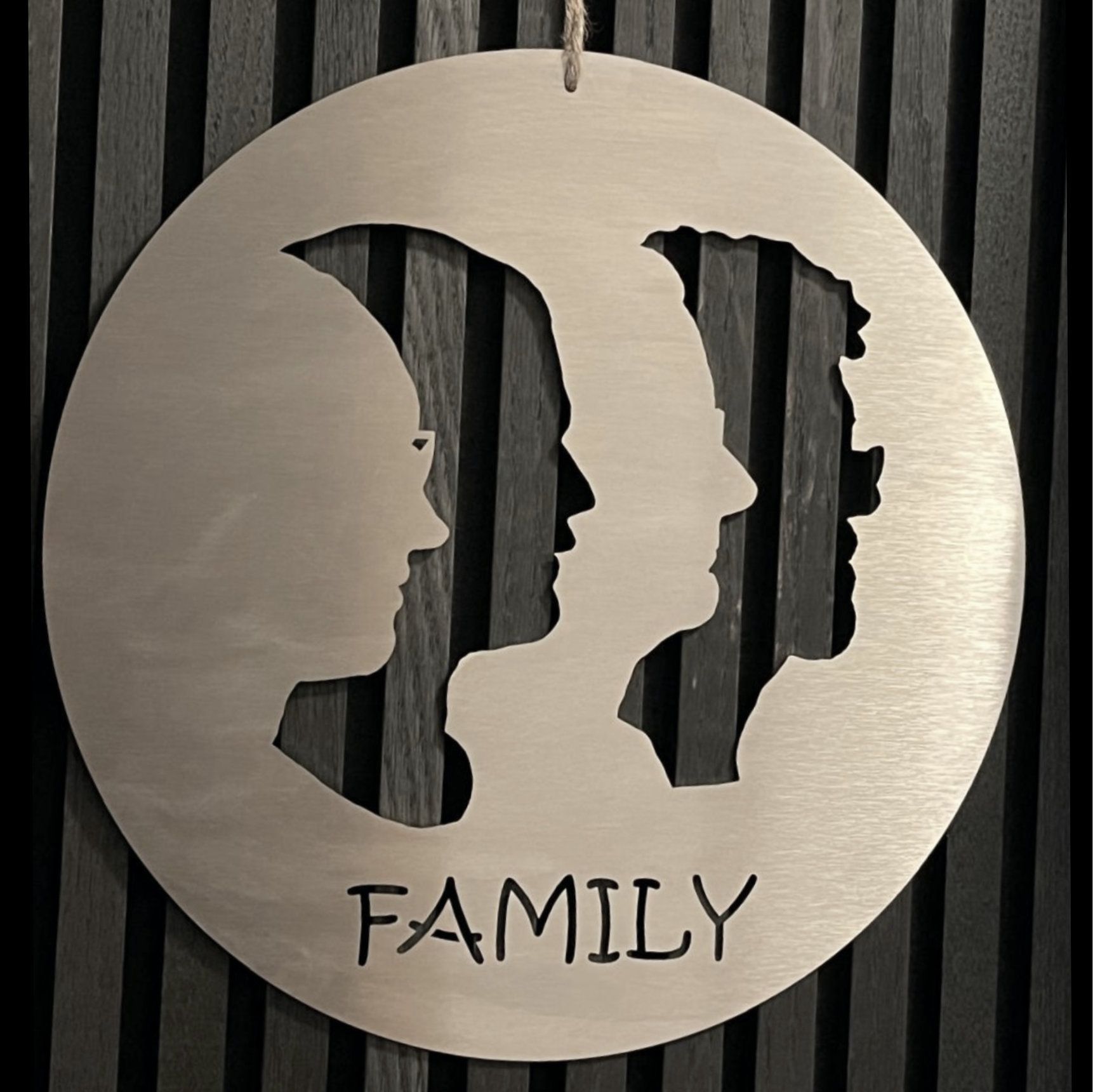 Rundes Wandbild aus Metall mit drei Profilsilhouetten und dem Wort „FAMILIE“ darunter.