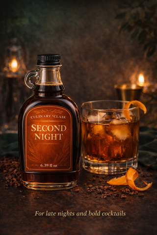 A bottle of Second Night amber liquid next to a cocktail on ice with an orange peel on a rustic, dimly lit table.
