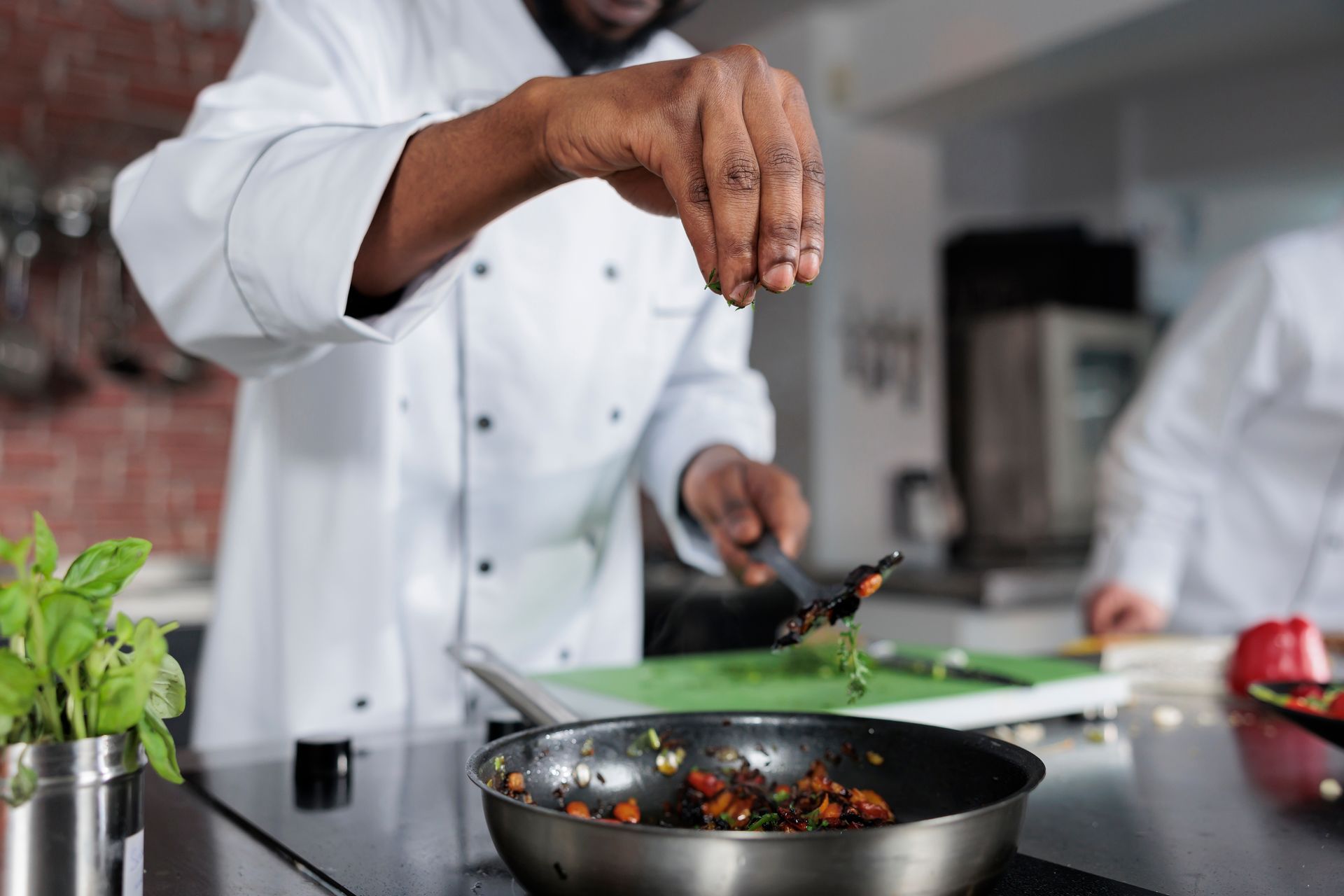 Chef seasoning food in a pan with herbs in a kitchen.
