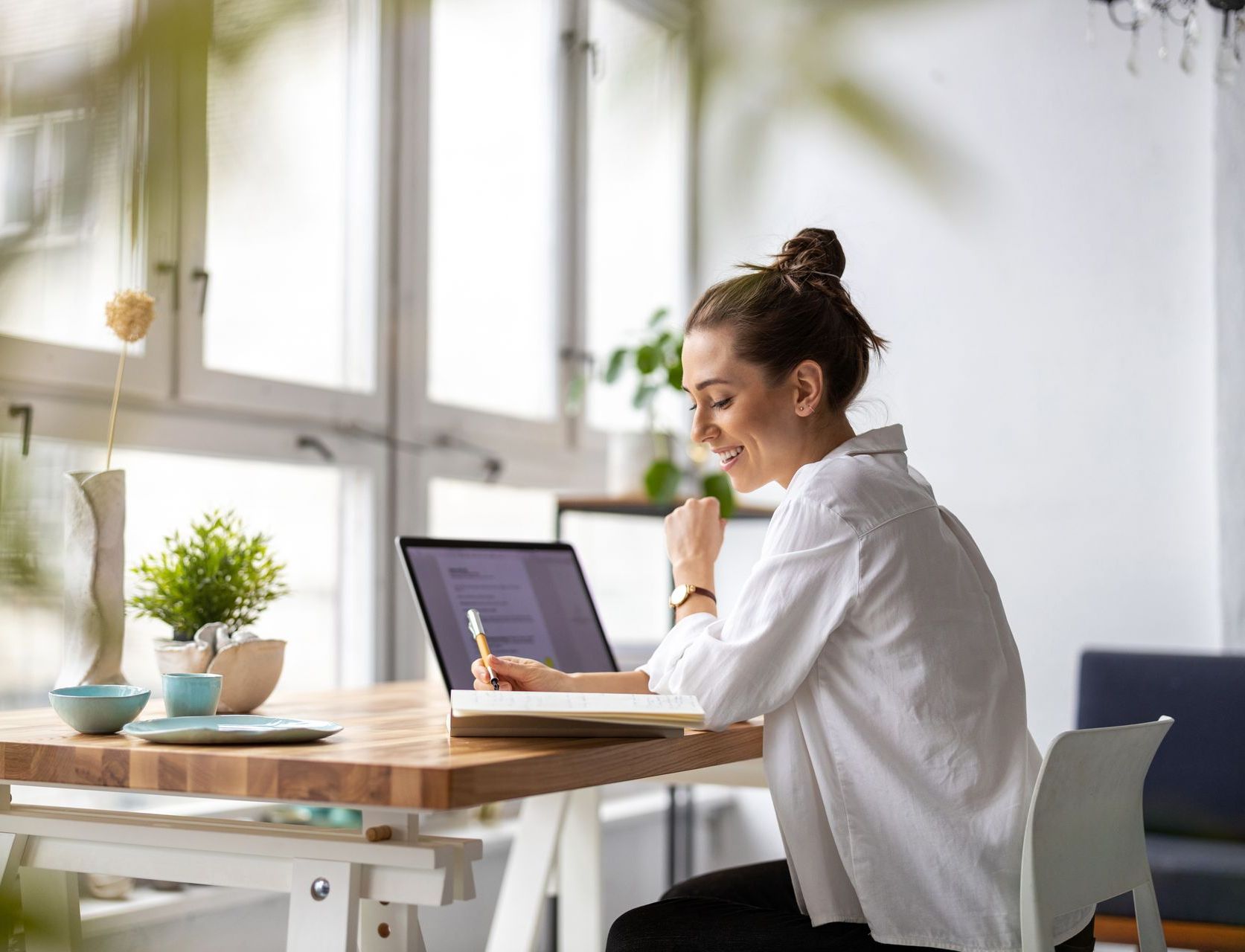 A woman taking notes from a laptop in front of a window