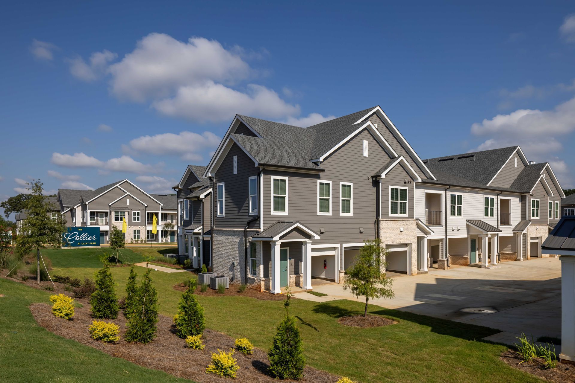 Townhouses with gray siding, white trim, and open garages under a blue sky.