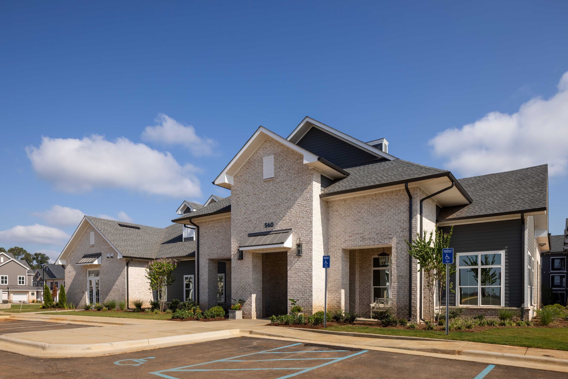 Light brick building with gray roof, windows, and blue accessible parking sign.