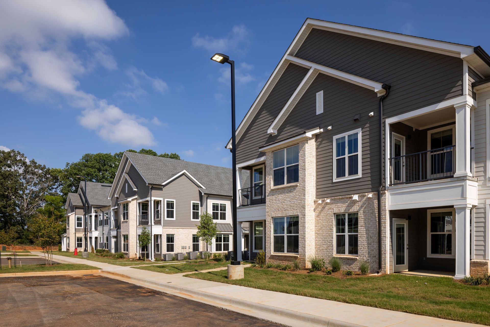 Row of new apartment buildings with gray siding, white trim, and balconies under a blue sky.