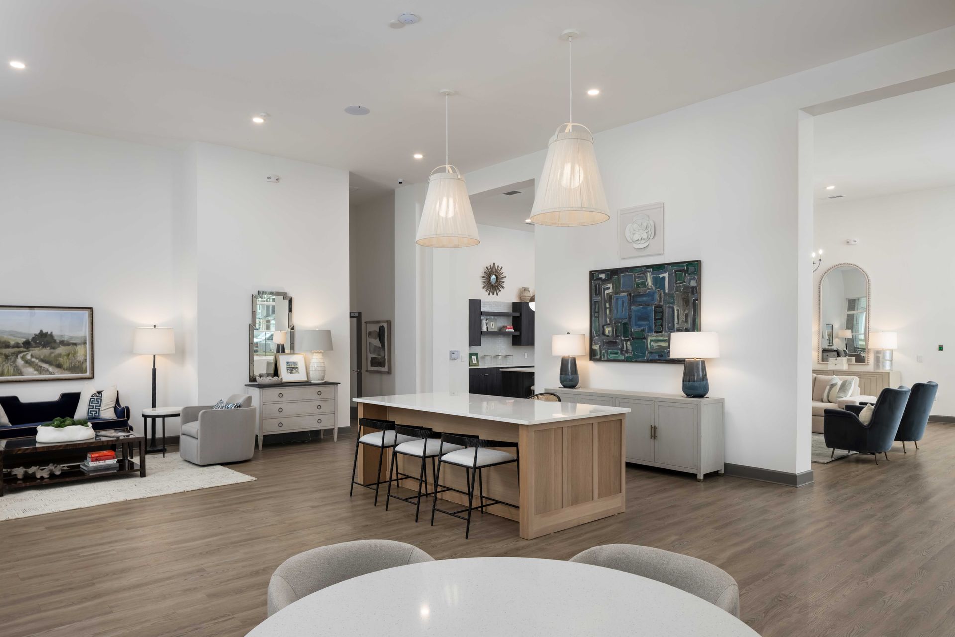 Lounge area with a kitchen, seating, and chandelier. White walls, wood floors.