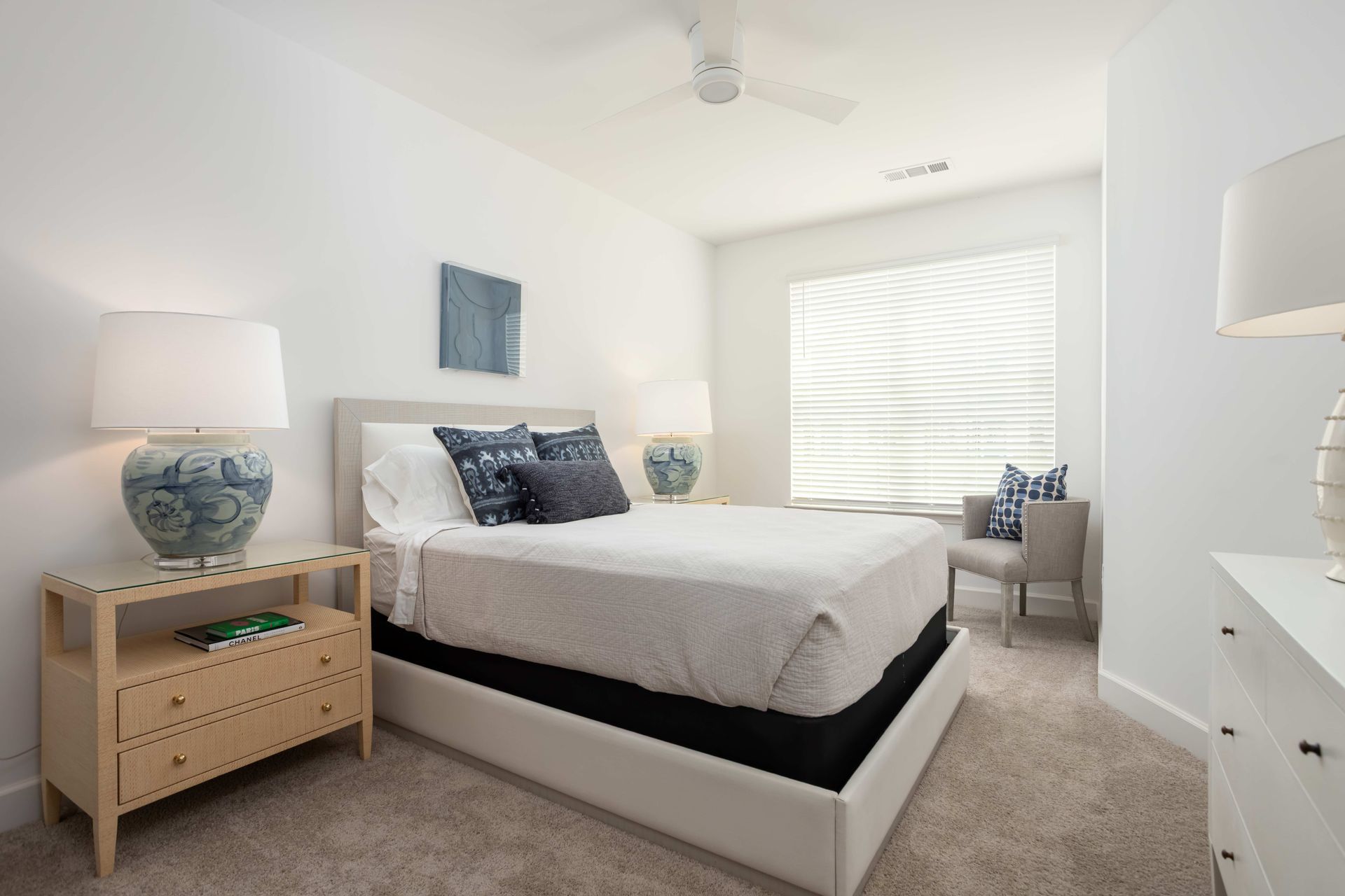 Bedroom with a white and blue color scheme; bed, bedside table with lamp, window, chair.