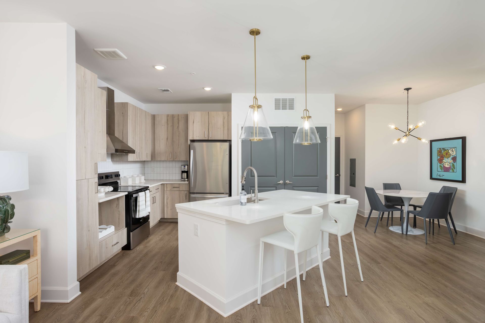 Modern kitchen with island and dining area; light wood cabinets, white island, gold pendant lights.