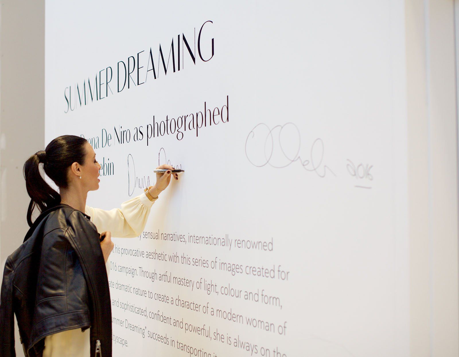 Drena De Niro autographs the artist’s statement wall; David Drebin’s autograph is seen to the right