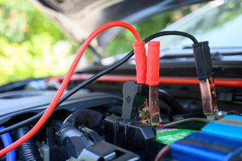 A close up of a car battery being charged with jumper cables.