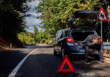 A man is sitting in the back of a broken down car.