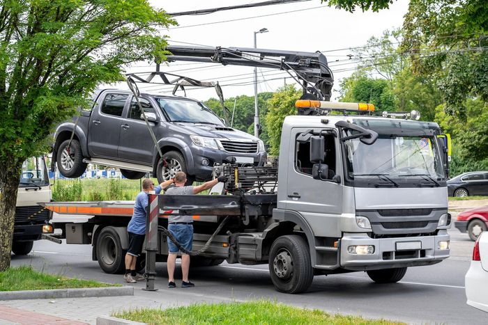 A tow truck is towing a pickup truck on a flatbed trailer.