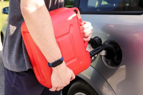 A man is holding a red gas can in front of a car.