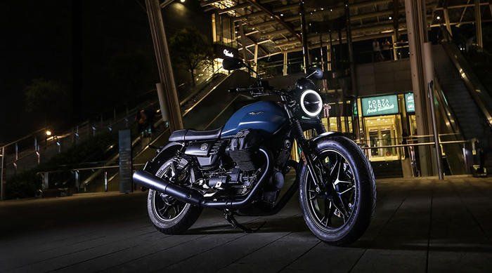 A blue motorcycle is parked in front of a building at night.