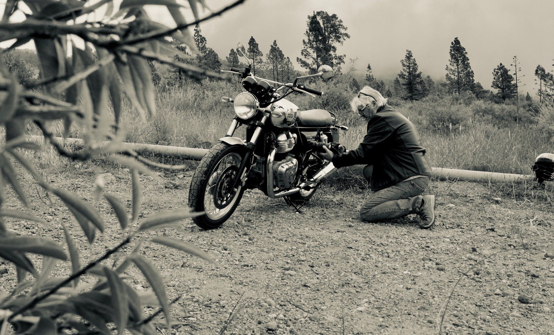 A man is kneeling down next to a motorcycle in a black and white photo.