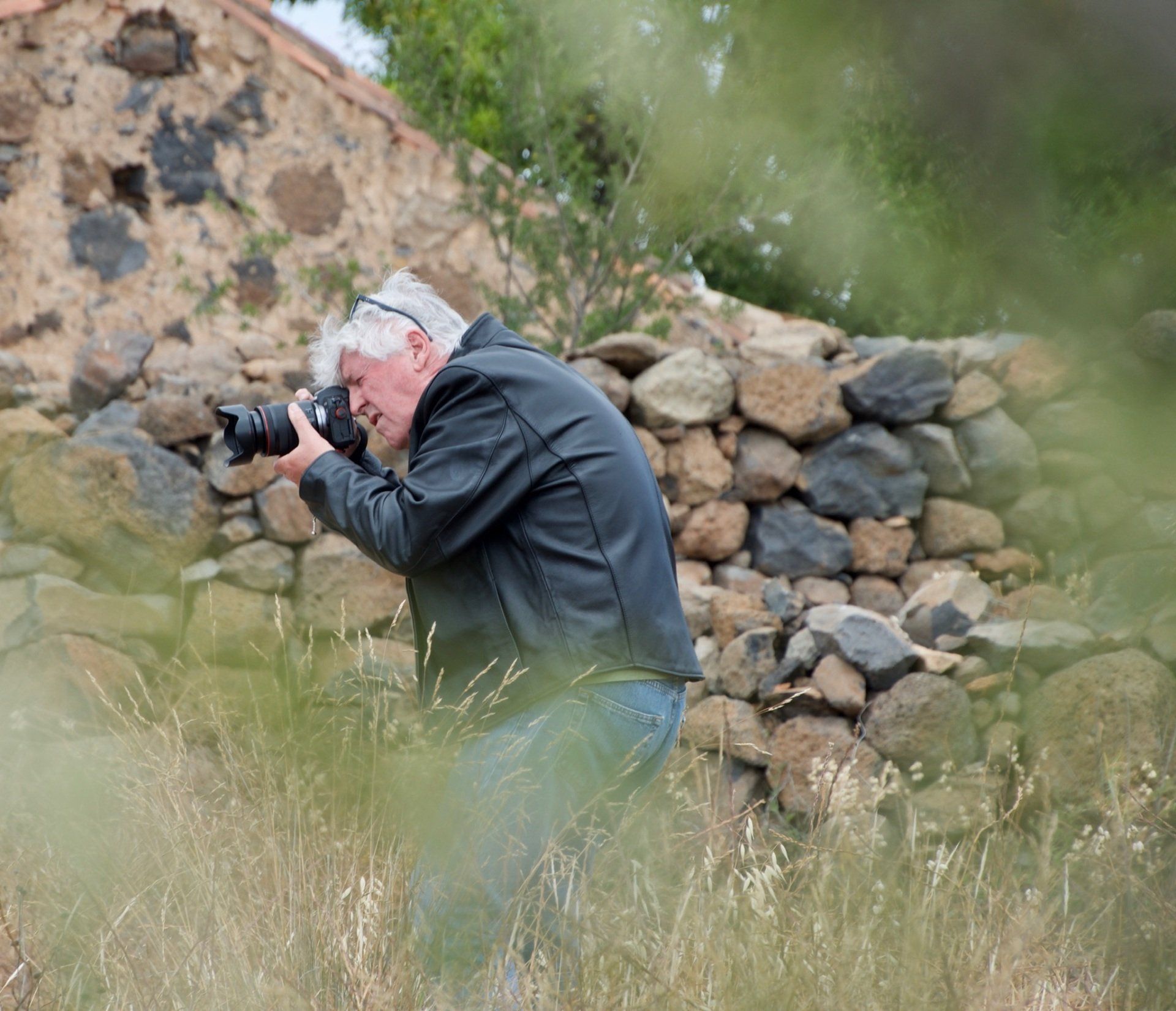 A man is taking a picture of a stone wall with a camera.