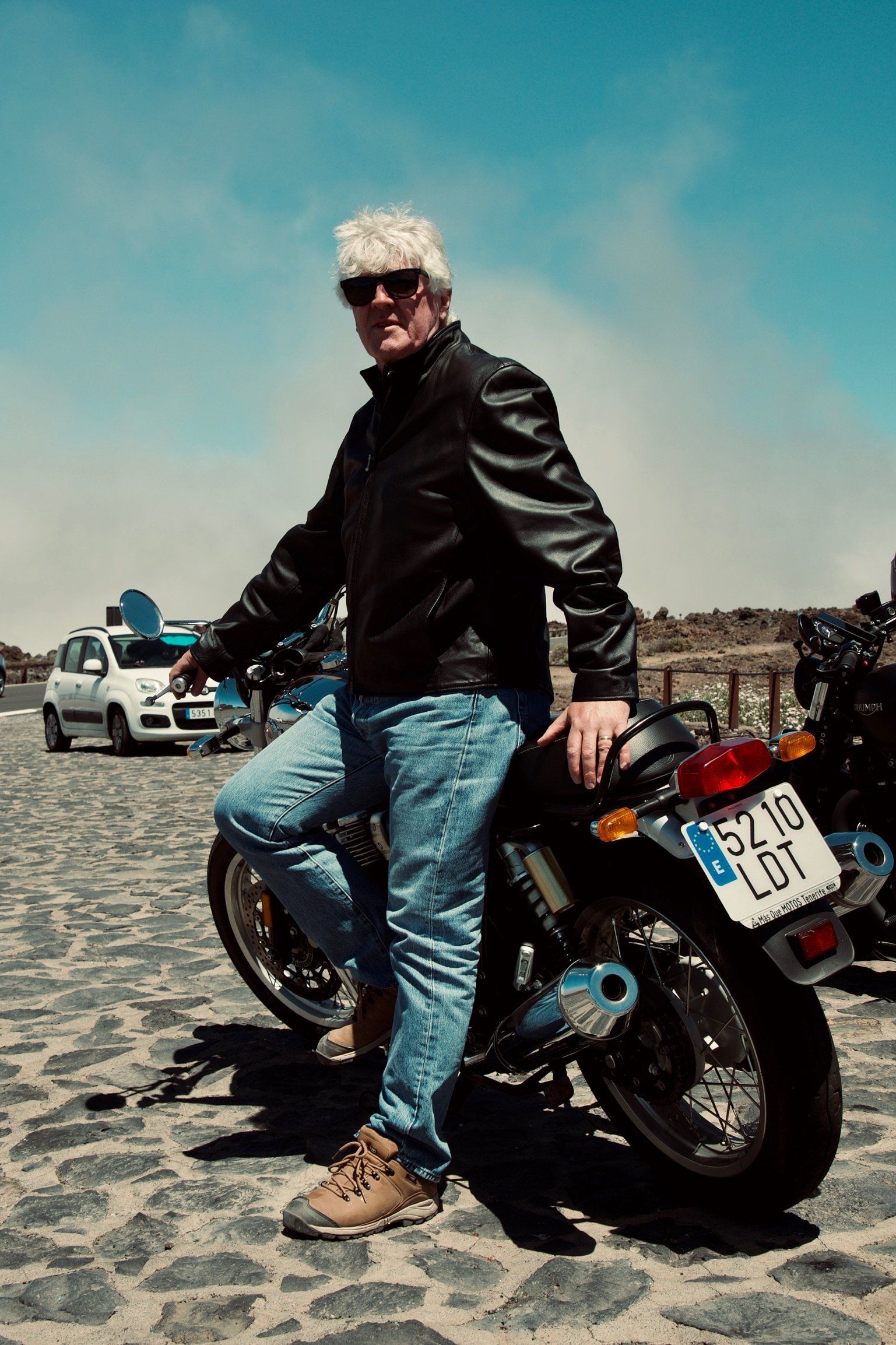 A man is leaning on a motorcycle on a cobblestone street.