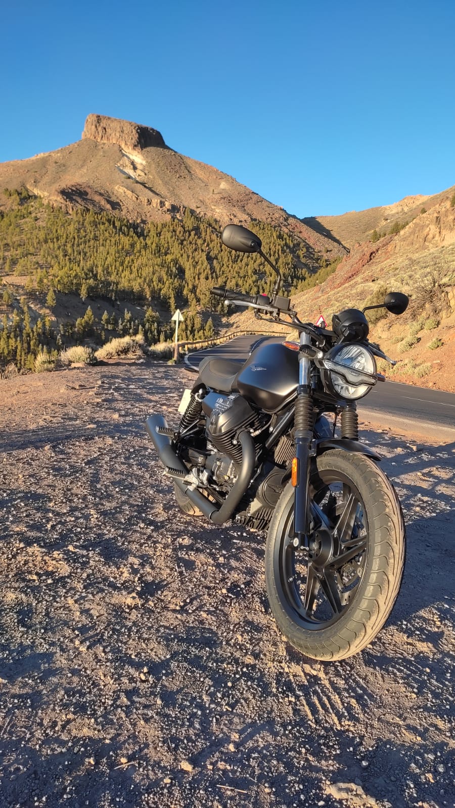 A motorcycle is parked on the side of a dirt road in front of a mountain.