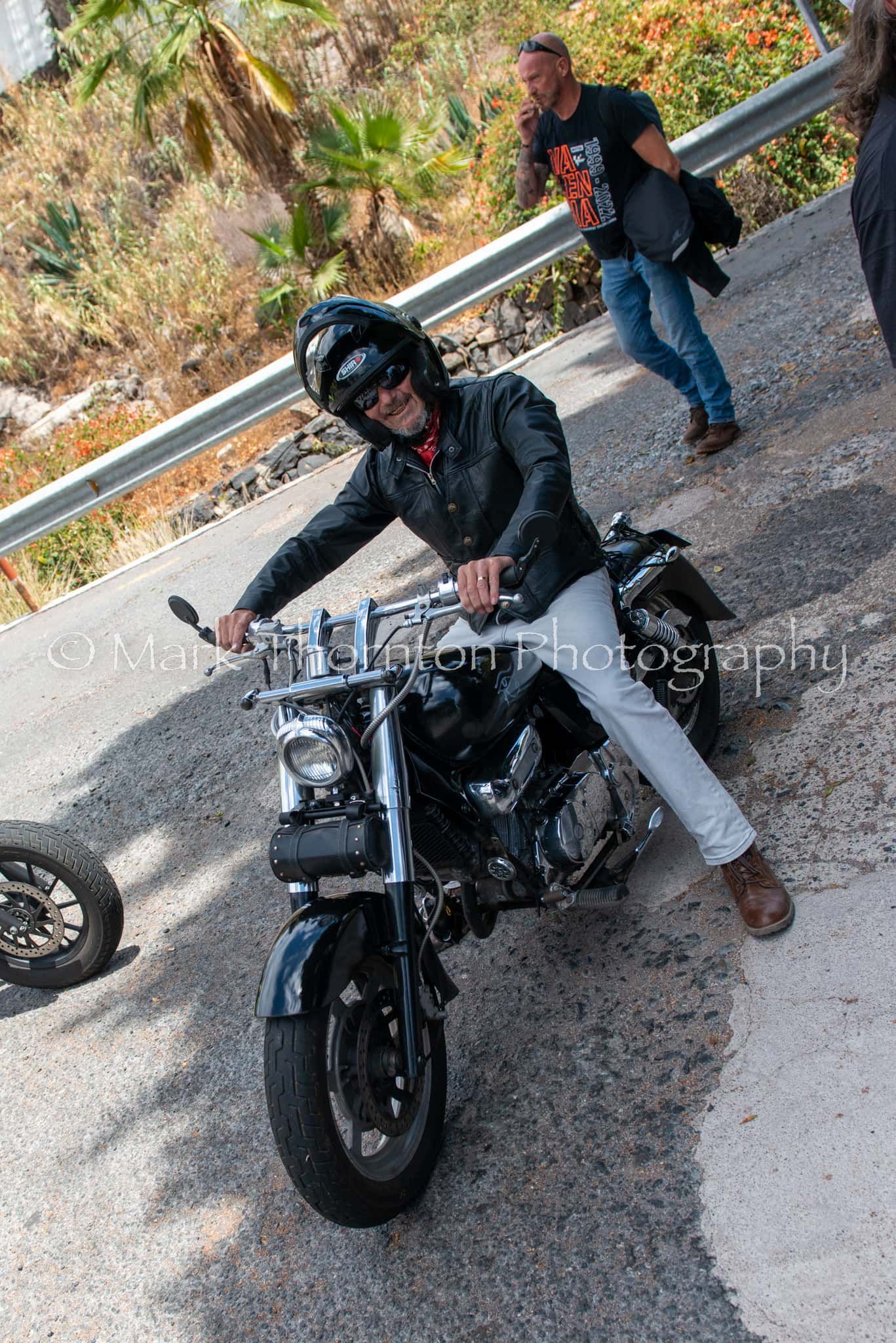 A man is sitting on a motorcycle on the side of the road.