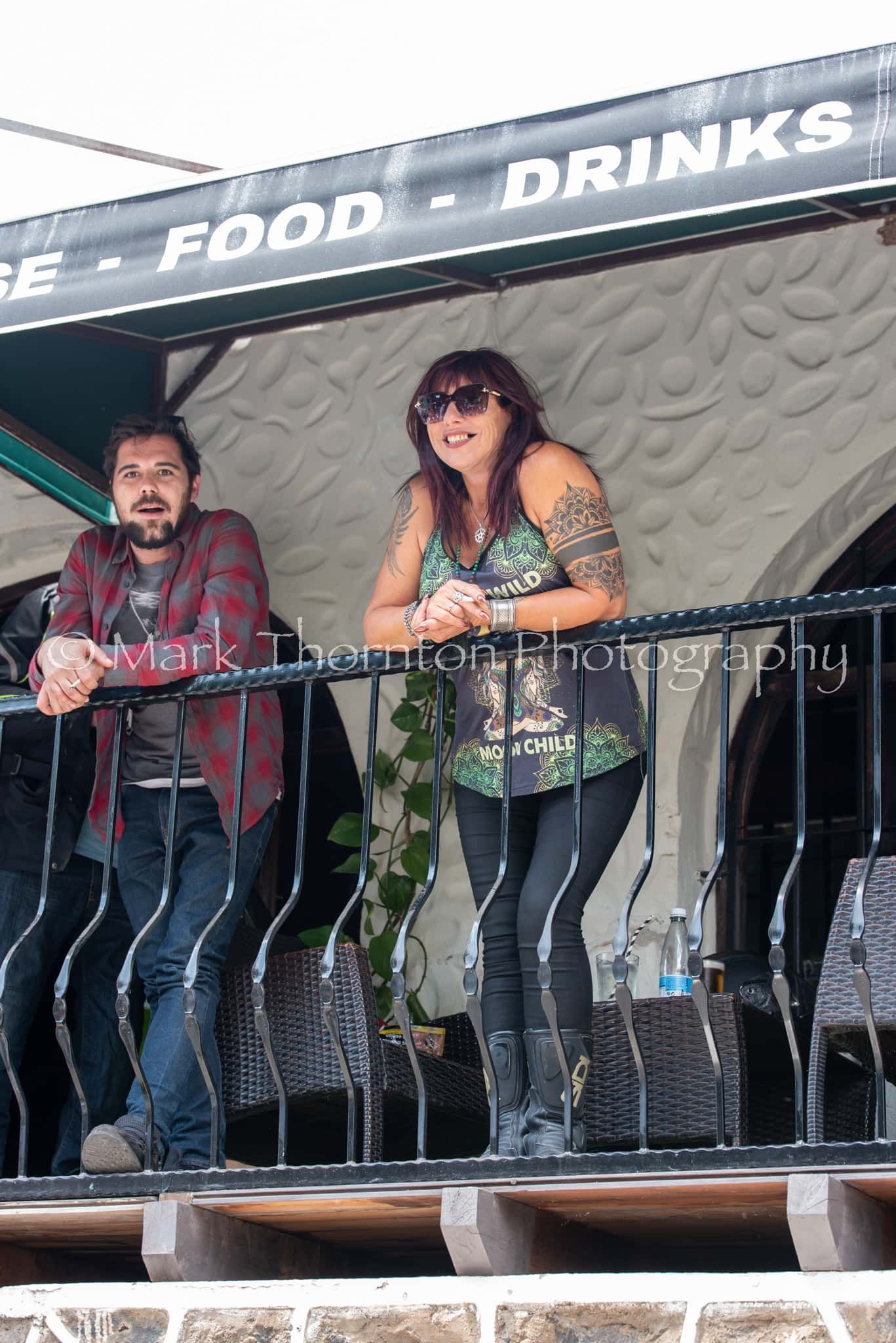 A man and a woman are standing on a balcony under a sign that says food drinks