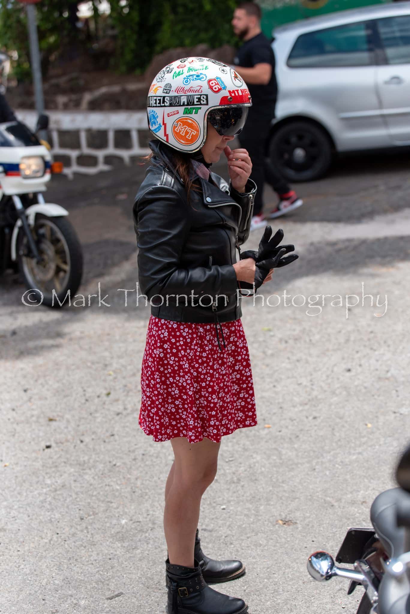 A woman wearing a helmet and a leather jacket is standing next to a motorcycle.