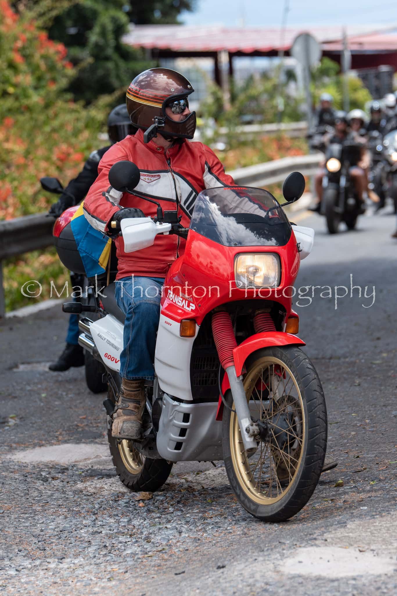 A man is riding a red and white motorcycle on a road.