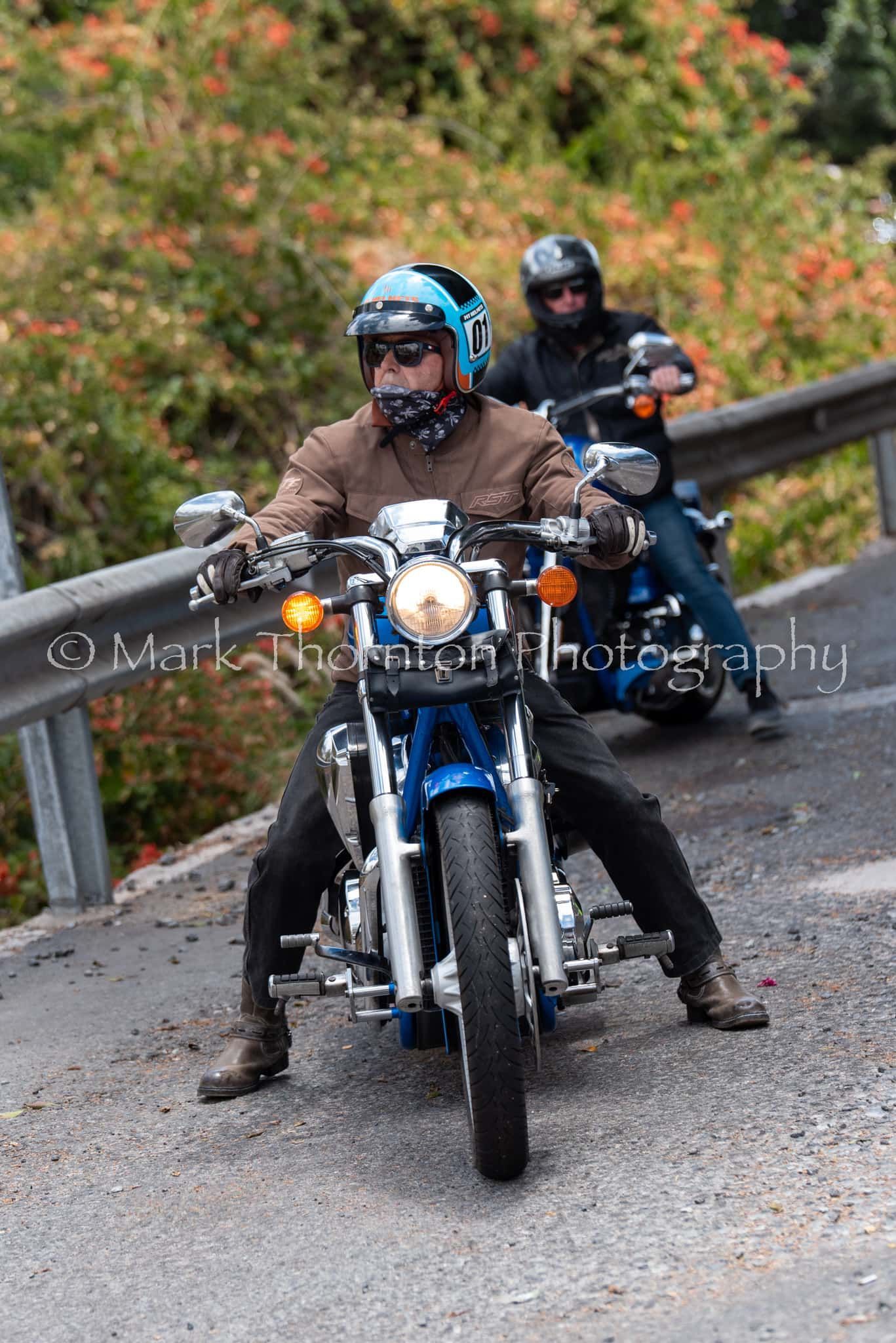 Two men are riding motorcycles down a road.