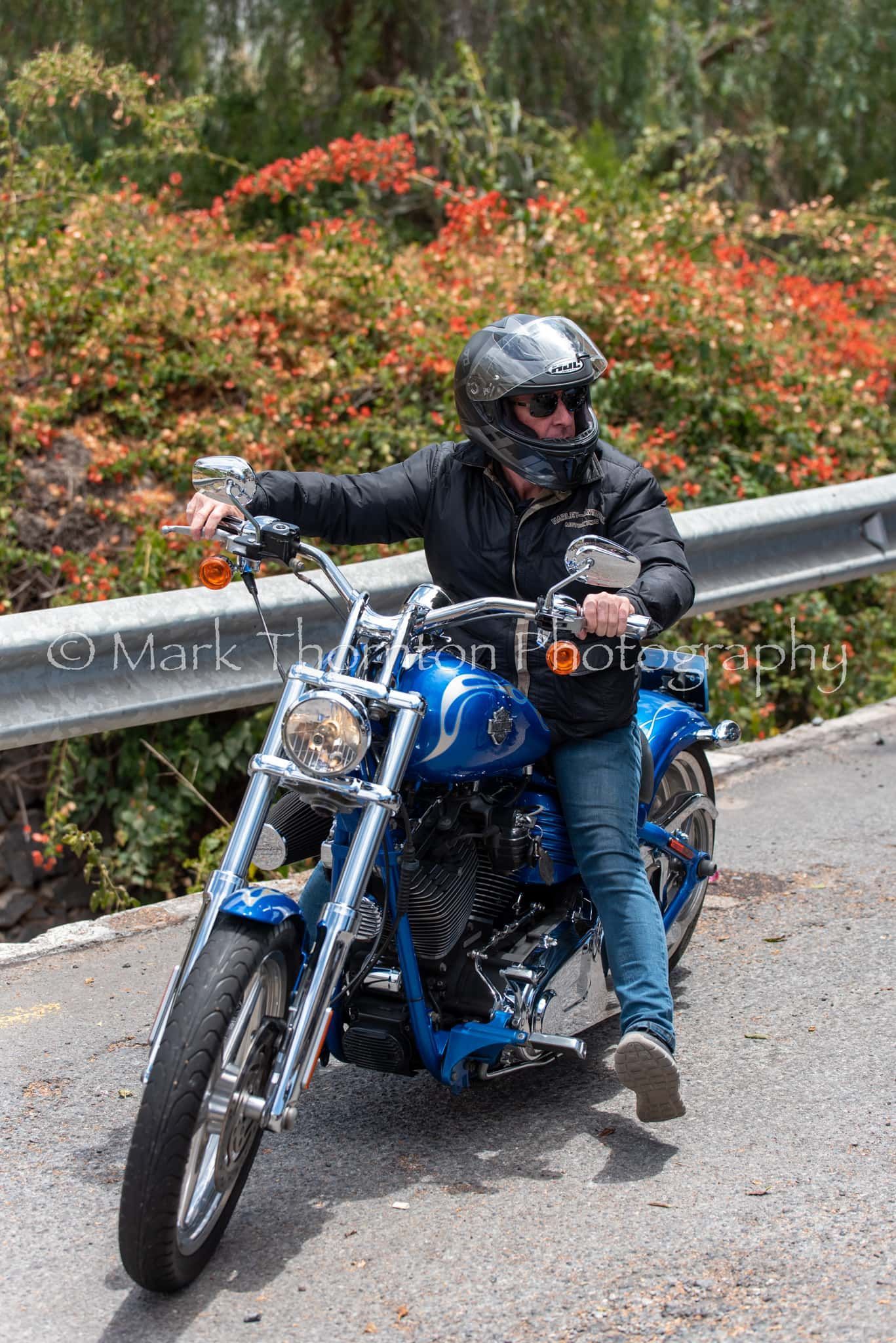 A man is riding a blue motorcycle down a road.