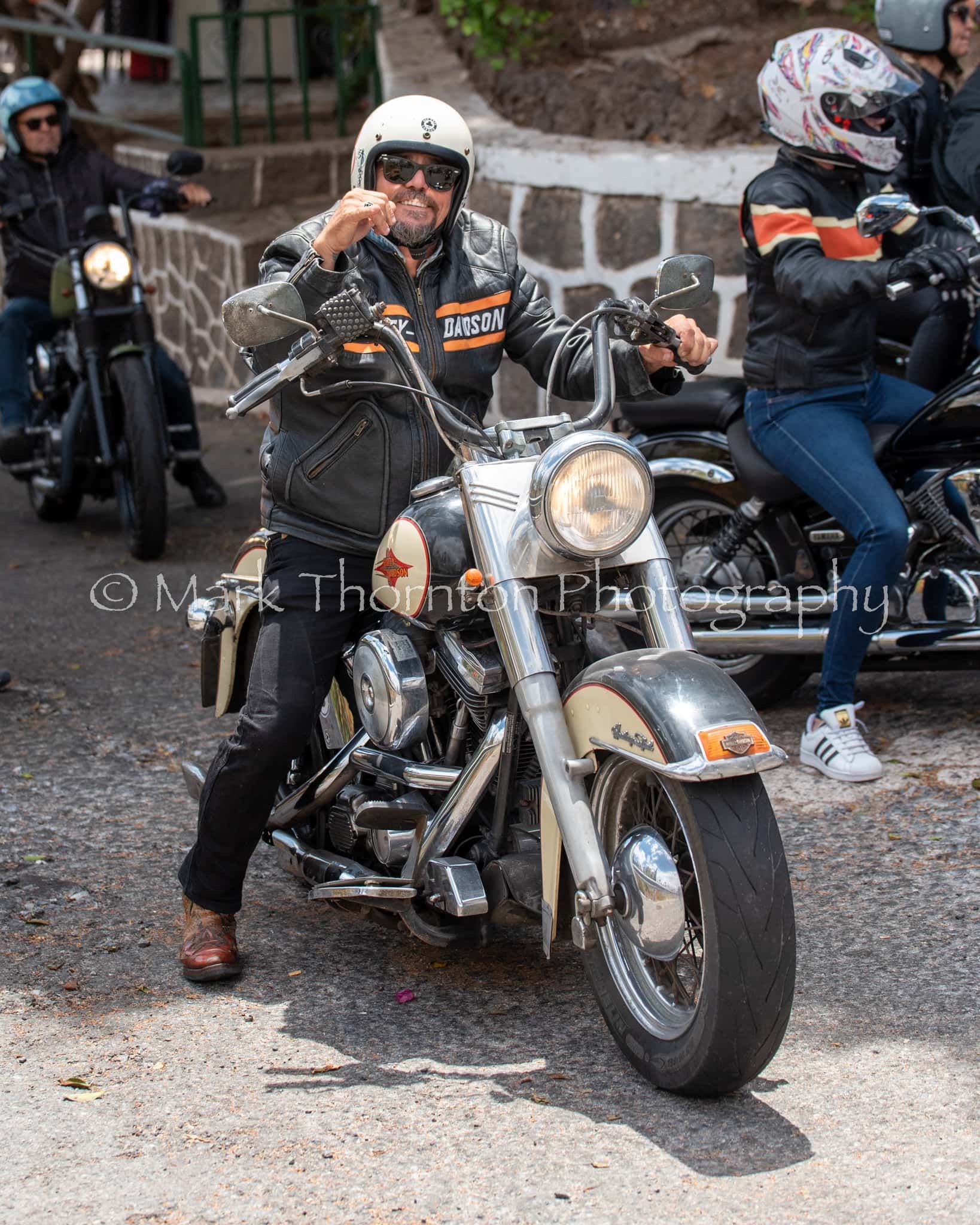 A man is standing on a motorcycle talking on a cell phone.