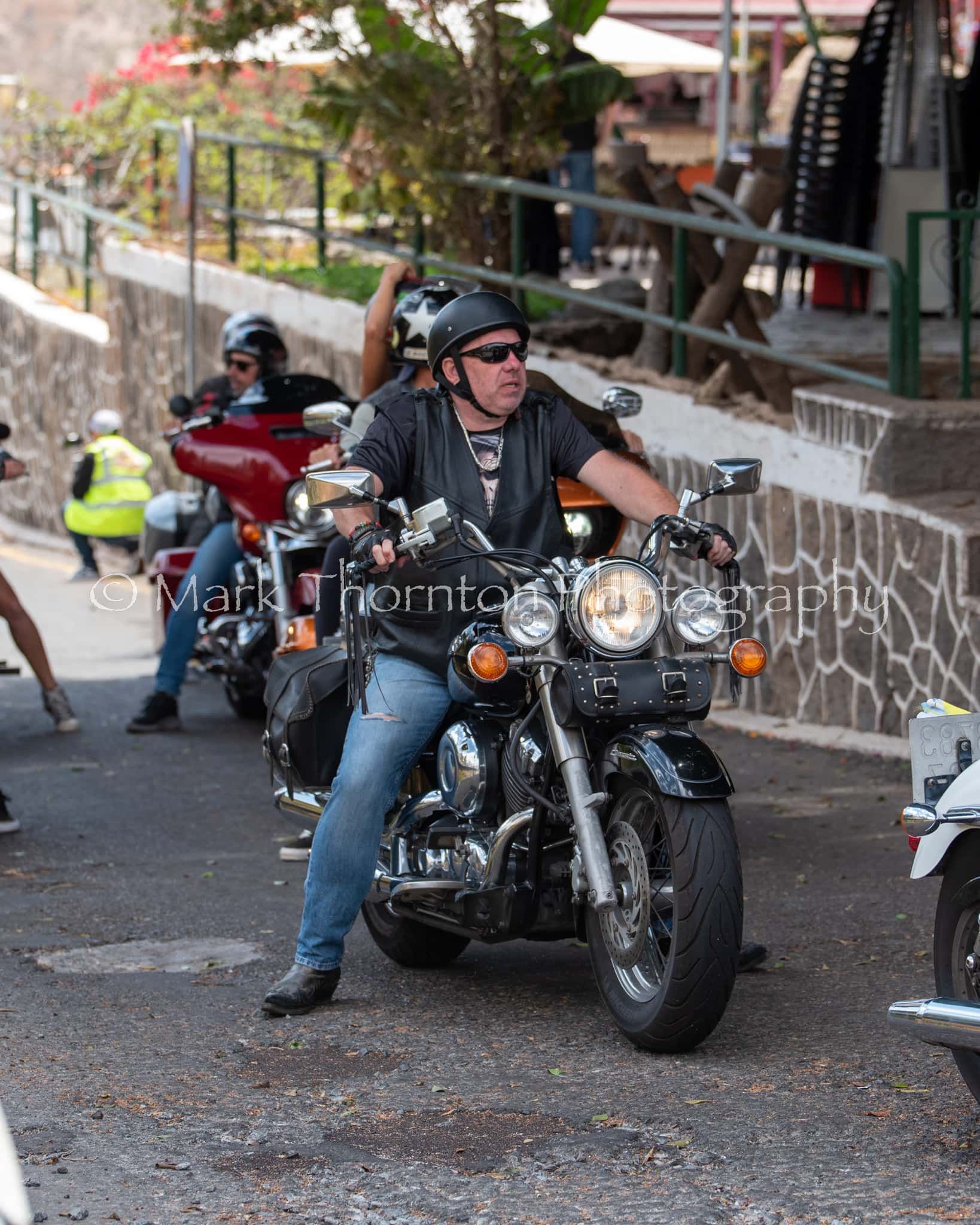 A man in a black leather jacket is riding a motorcycle