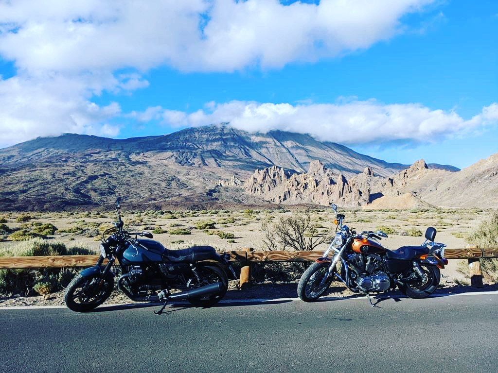 Two motorcycles are parked on the side of a road with mountains in the background
