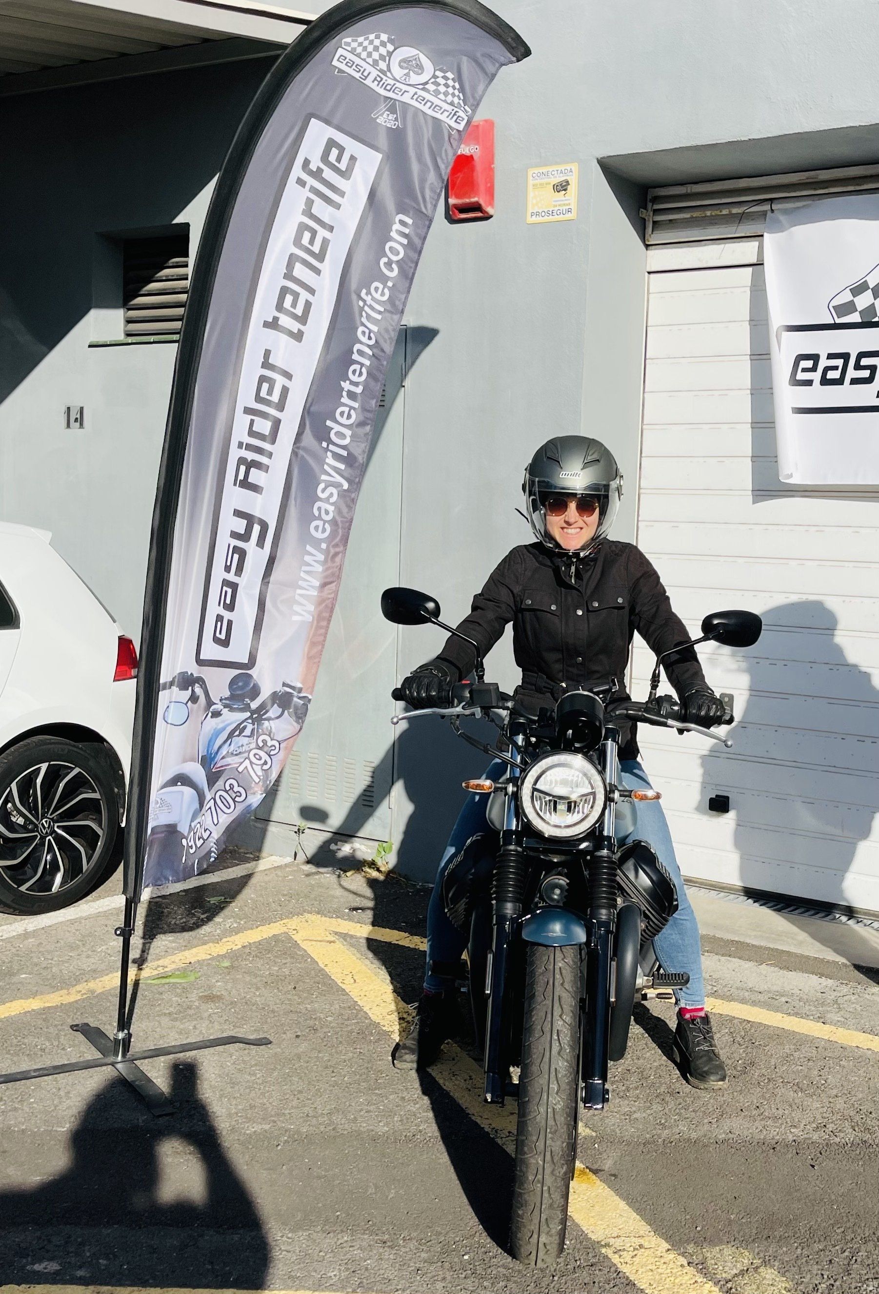 A woman is riding a motorcycle in a parking lot.