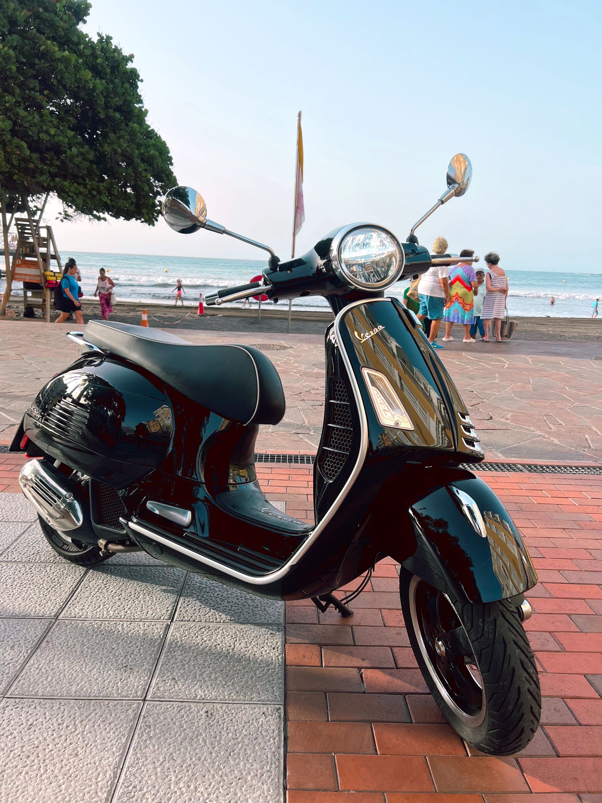 A black scooter is parked in front of a beach