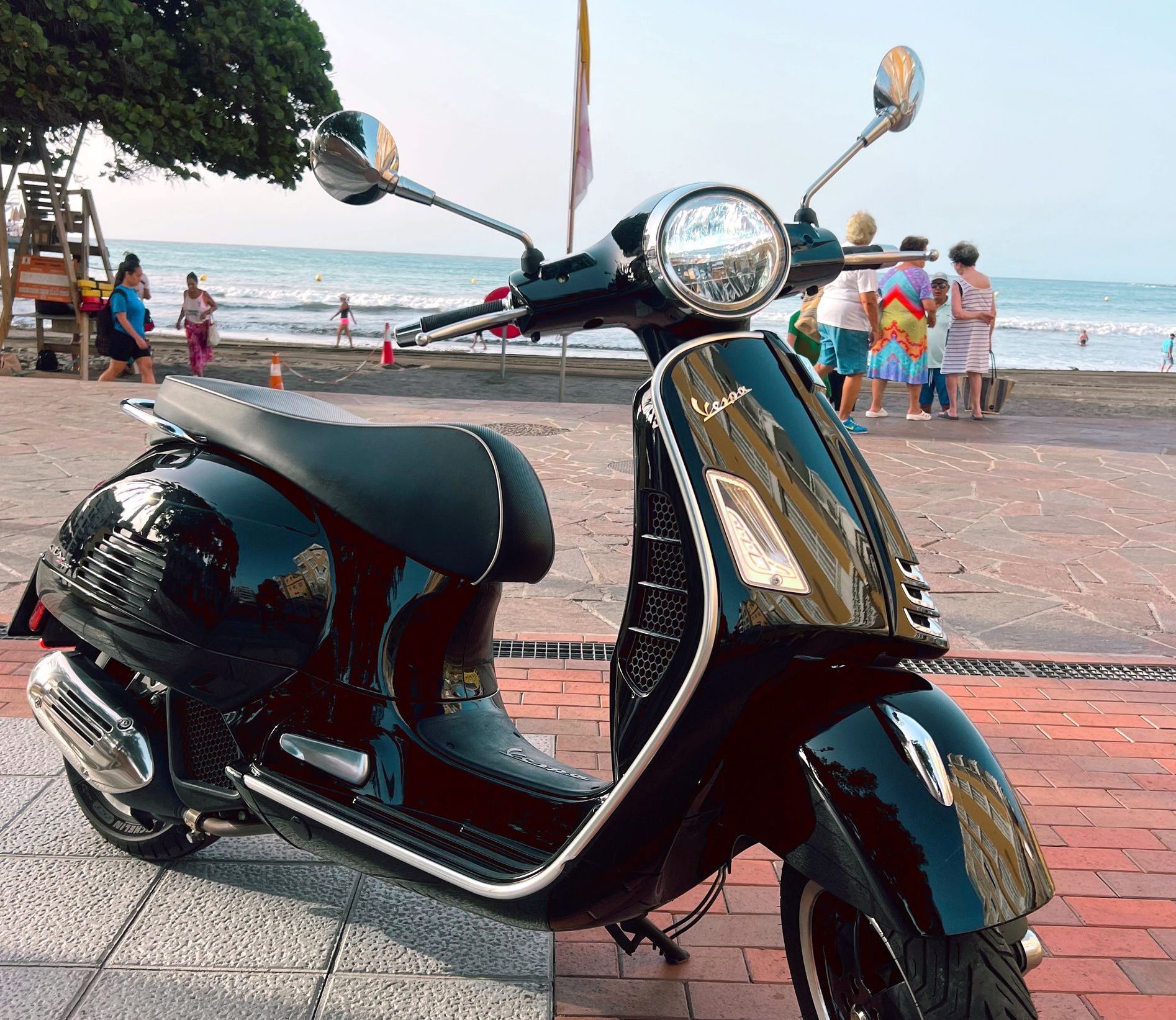 A black scooter is parked in front of a beach