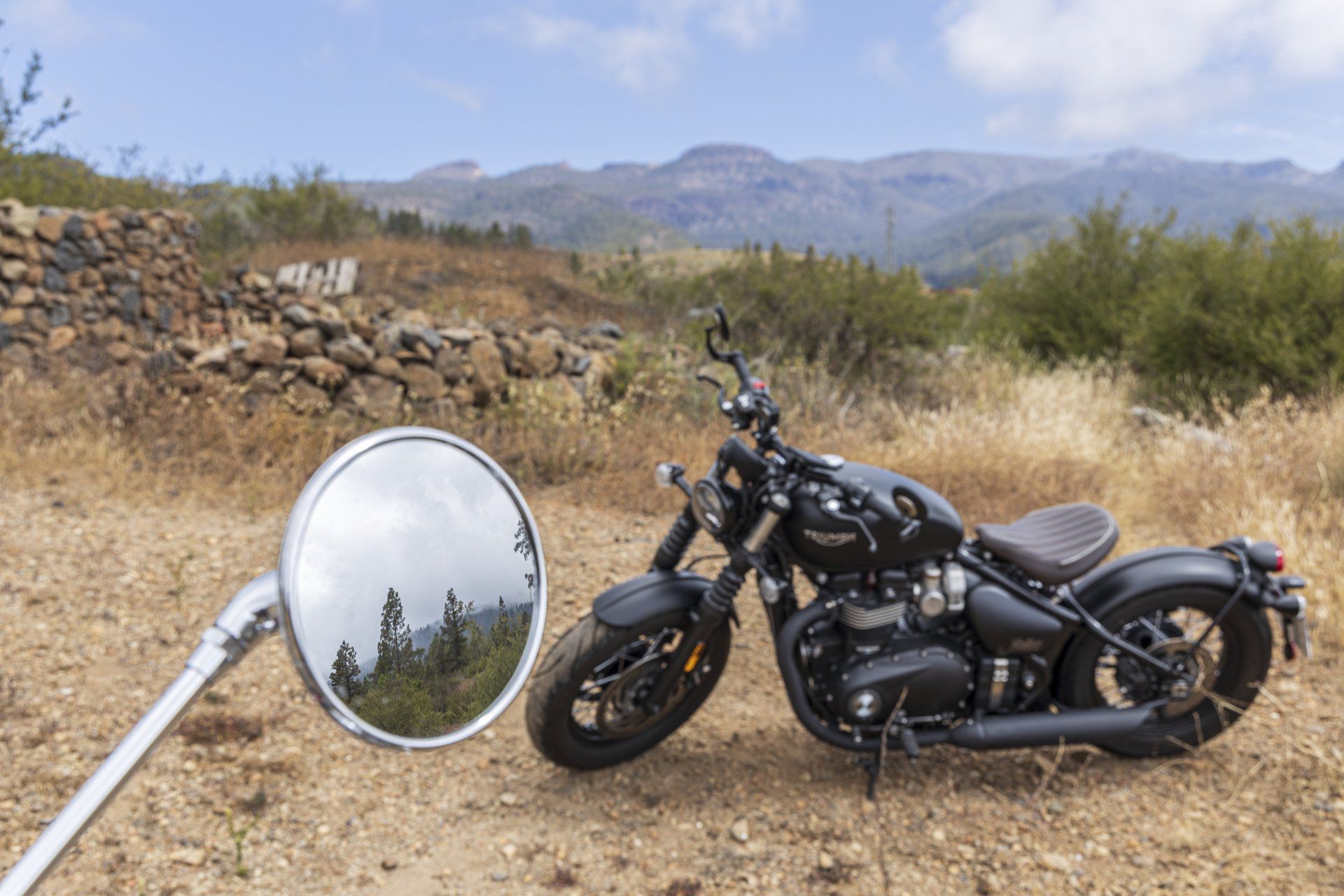 A motorcycle is parked in a dirt field with mountains in the background.