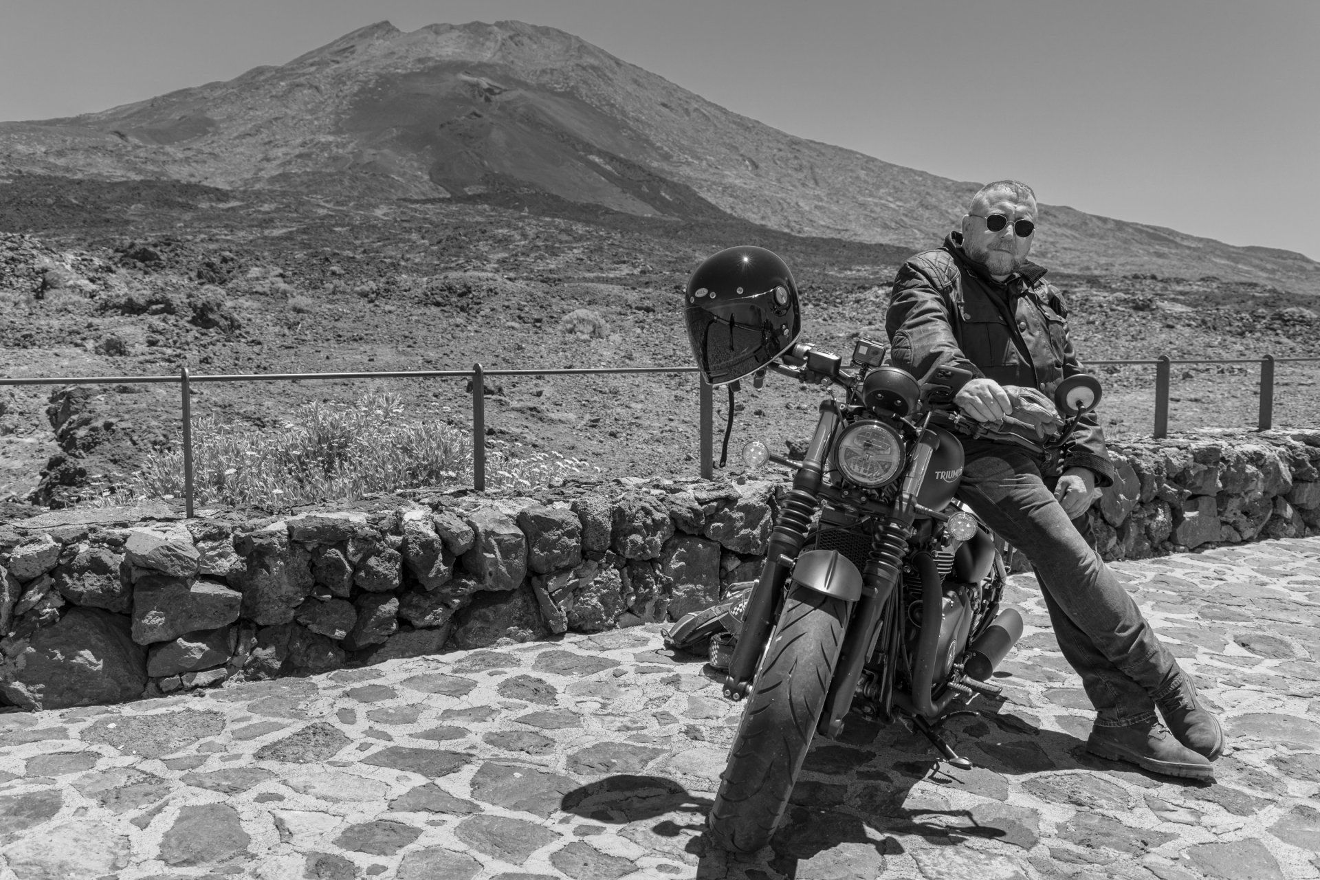 A man is sitting on a motorcycle with a mountain in the background.