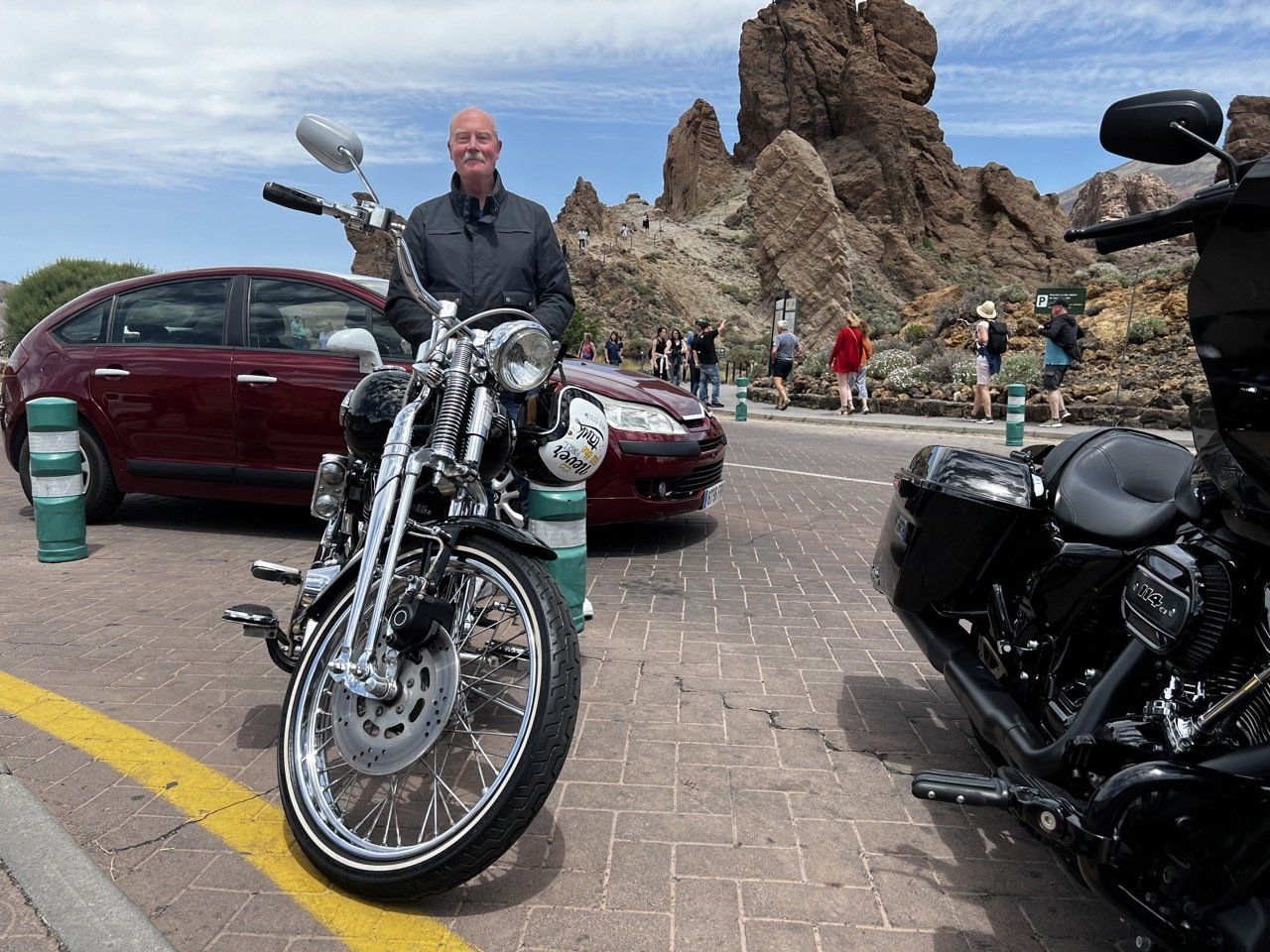 A man is standing next to a motorcycle and a car.