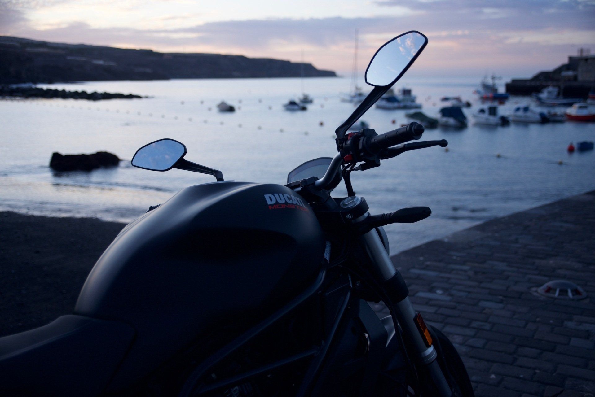 A motorcycle is parked on the side of the road near the water