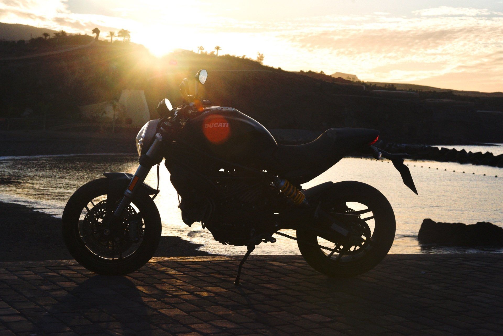 A motorcycle is parked on the side of the road near the water at sunset