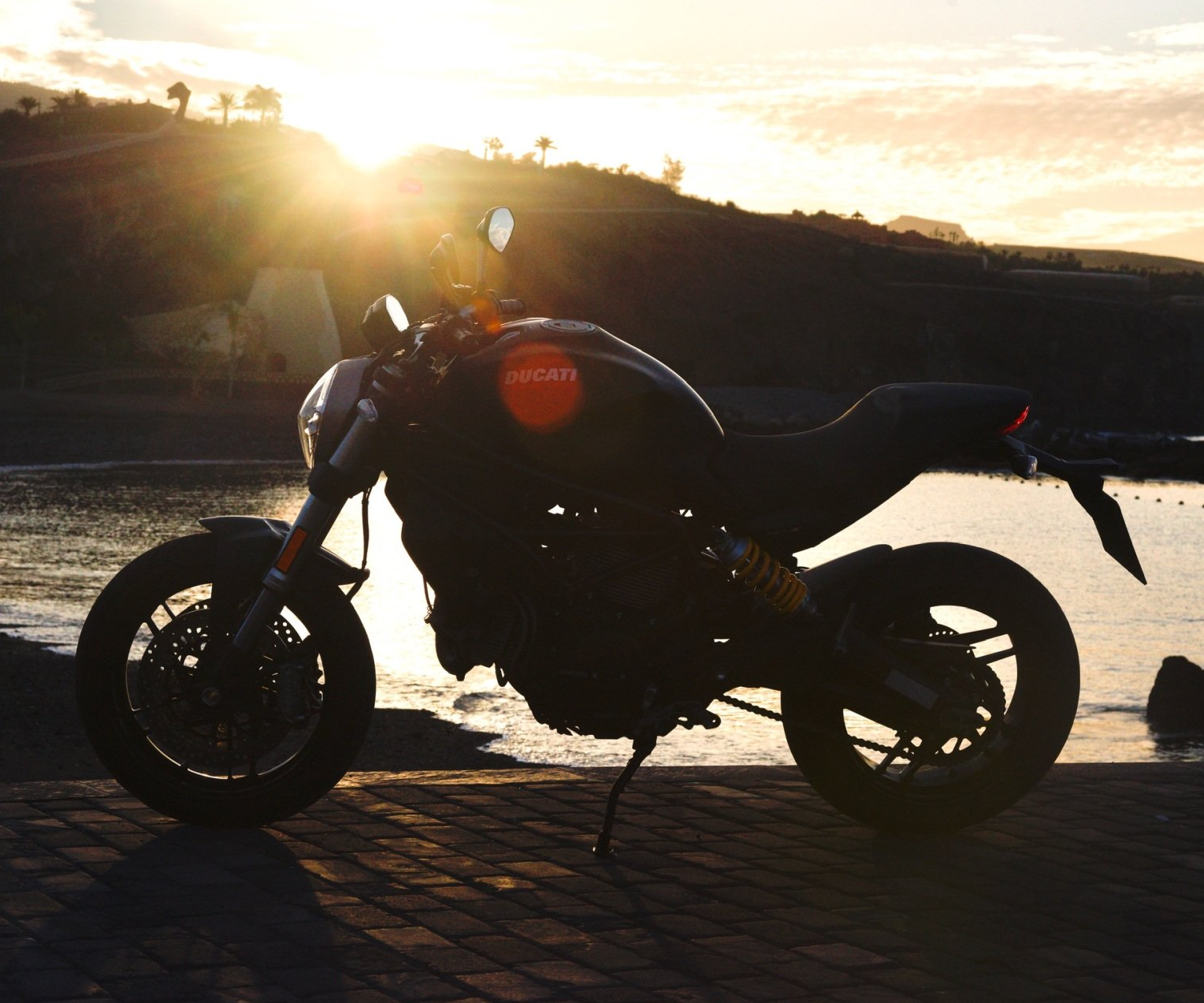 A ducati motorcycle is parked by the water at sunset