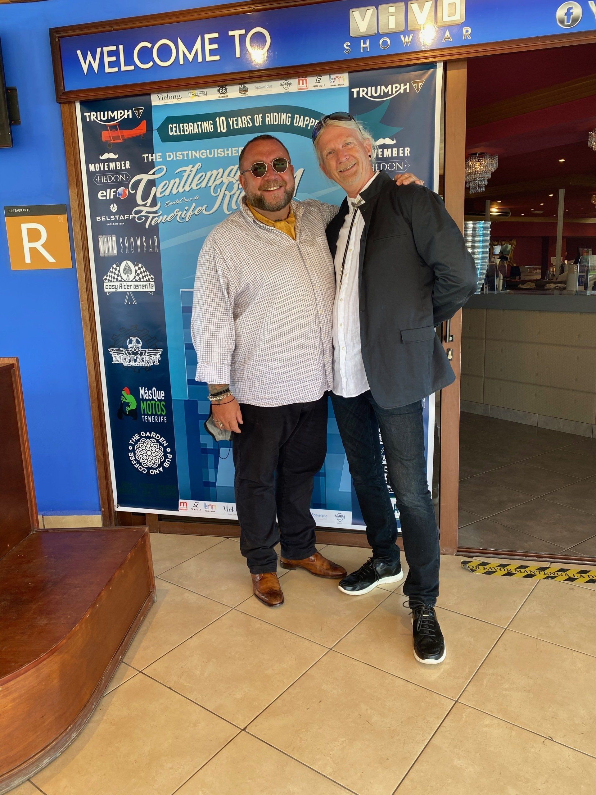 Two men are posing for a picture in front of a welcome sign