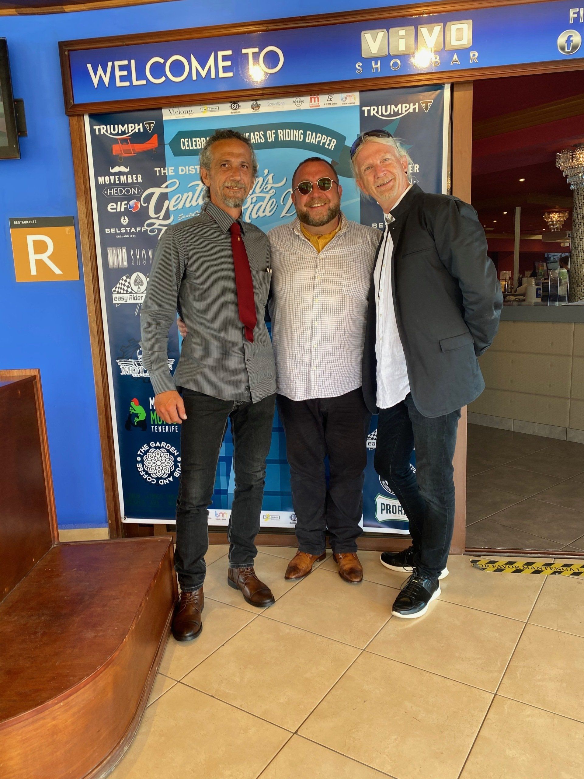 Three men are posing for a picture in front of a welcome sign.