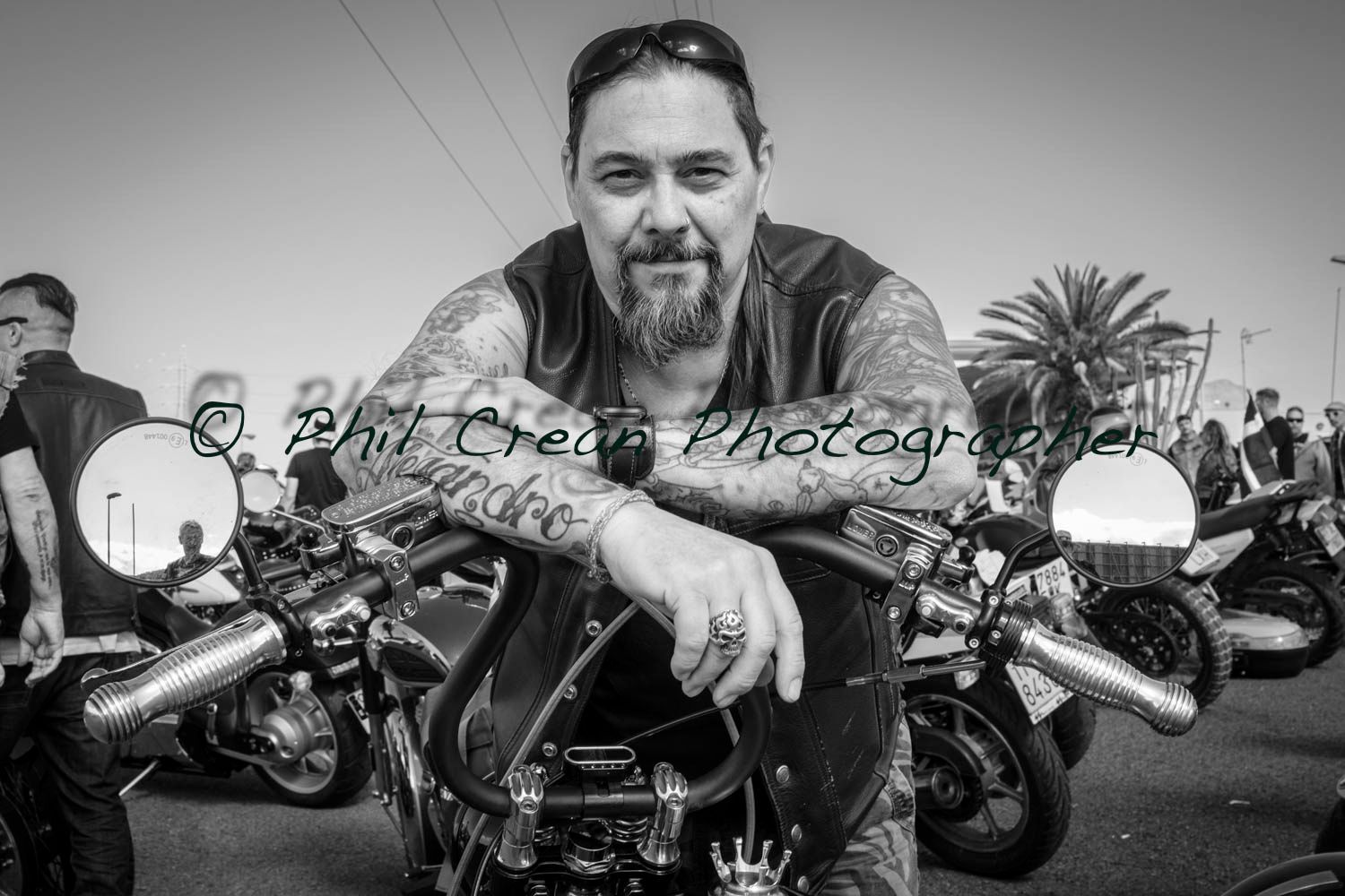 A man with a beard is sitting on a motorcycle in a black and white photo.