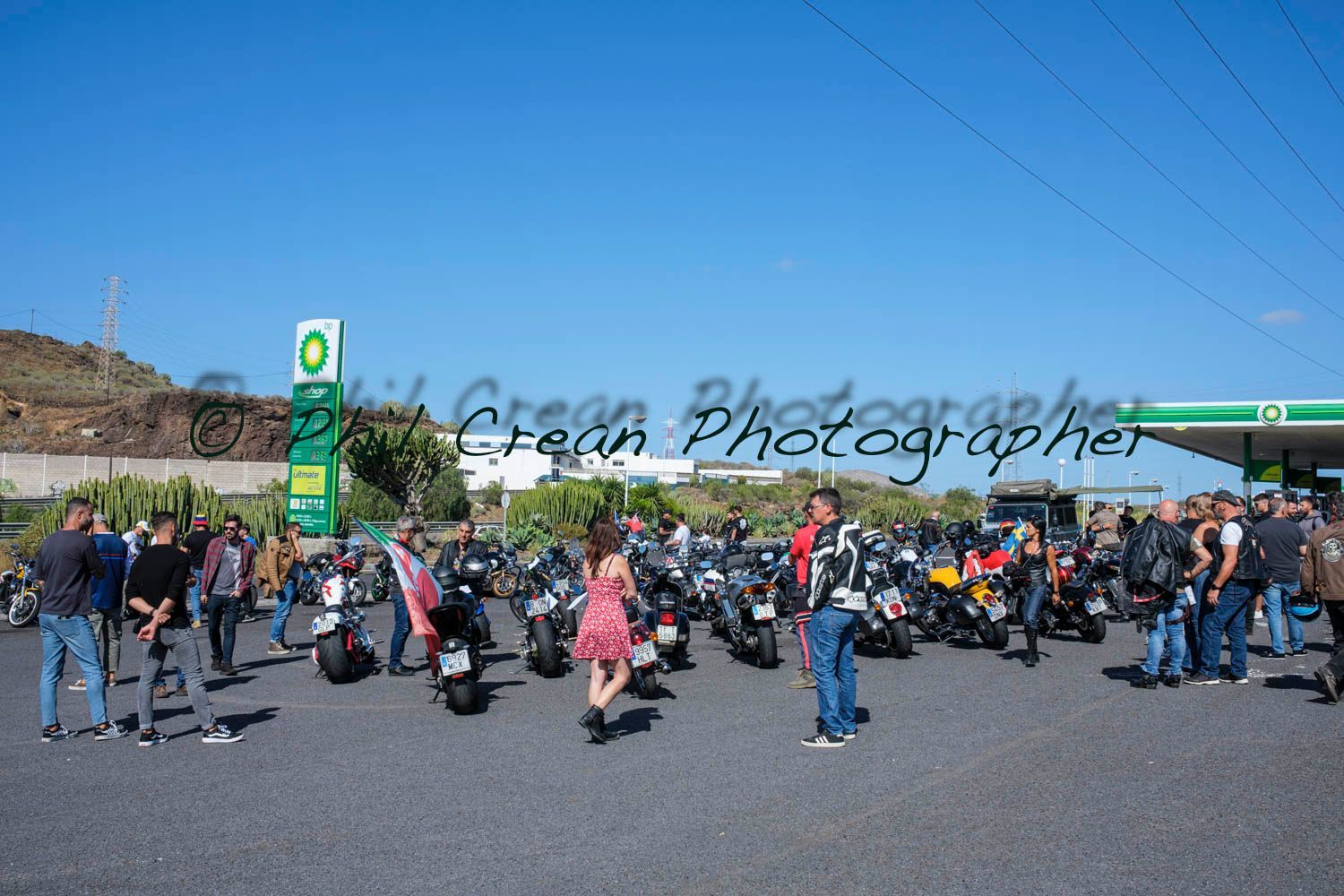A group of people are standing around motorcycles in a parking lot.