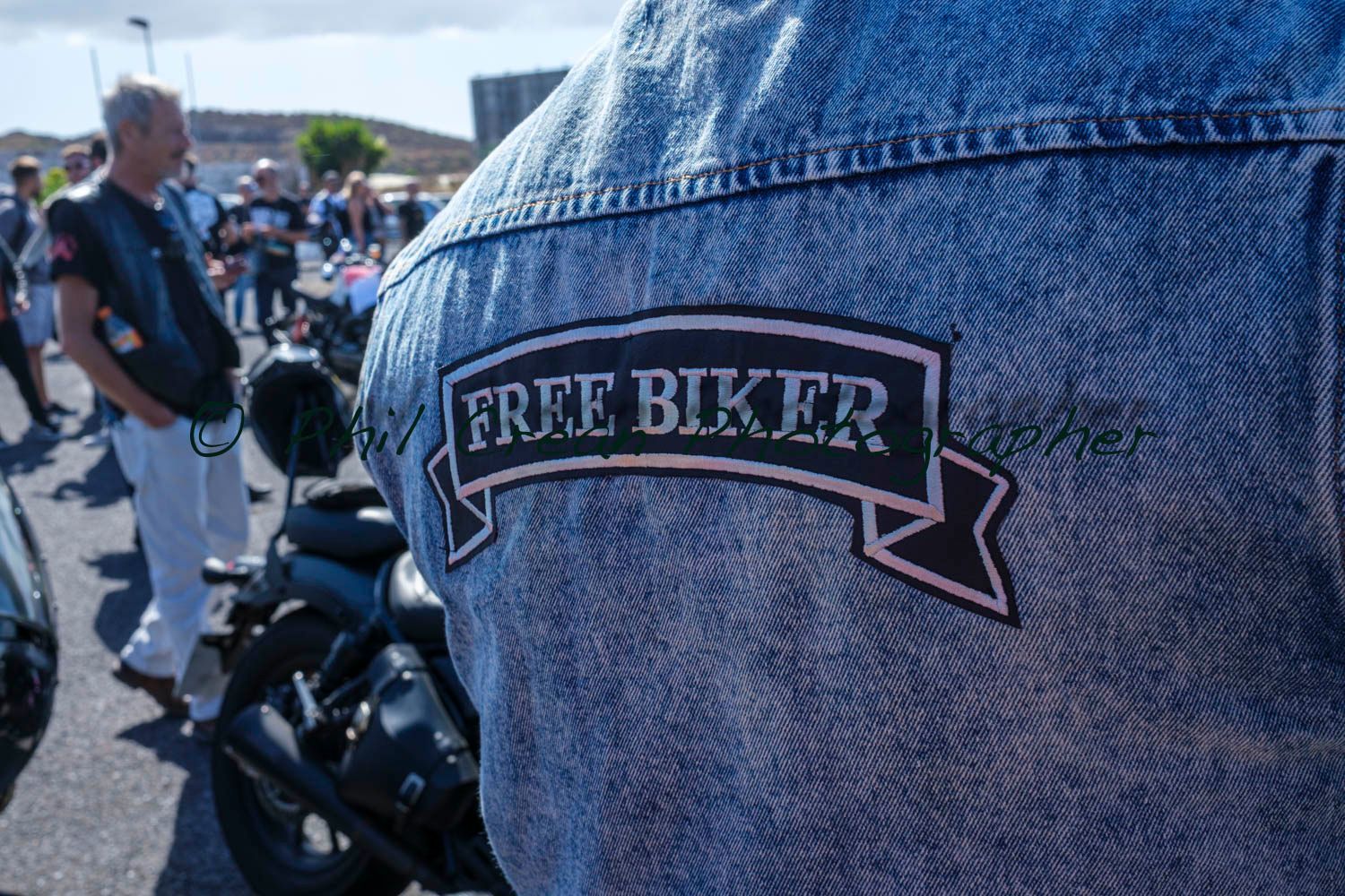 A man is wearing a denim jacket with a free biker patch on the back.