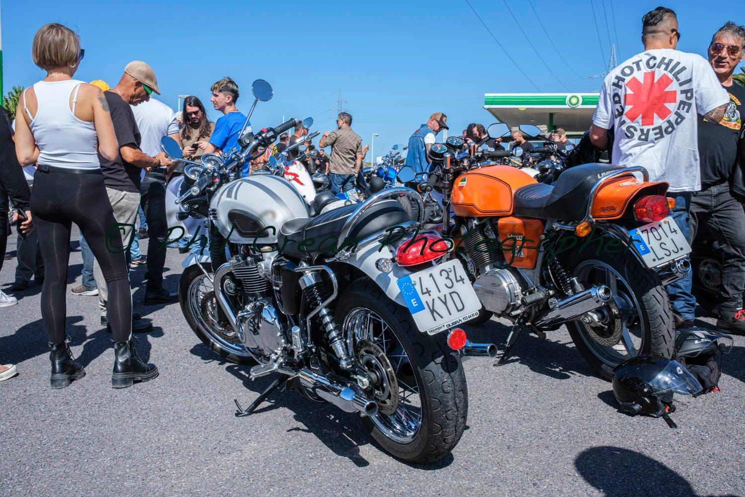 A group of people are standing around motorcycles in a parking lot.