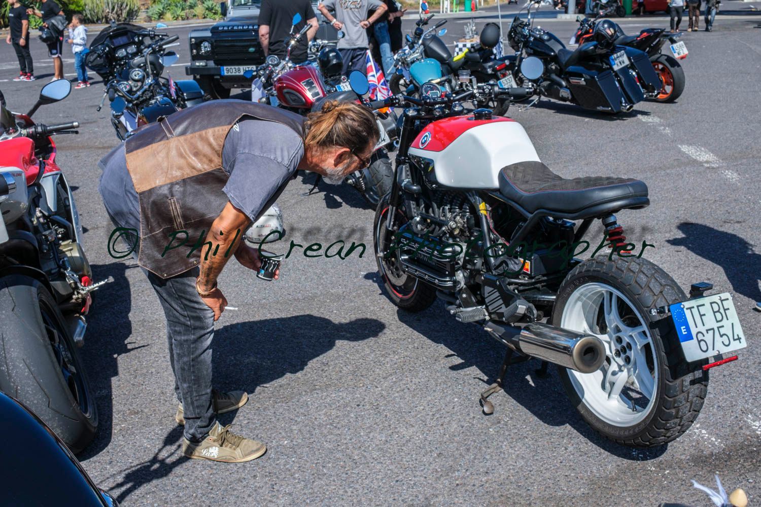 A man is bending over to look at a motorcycle in a parking lot.