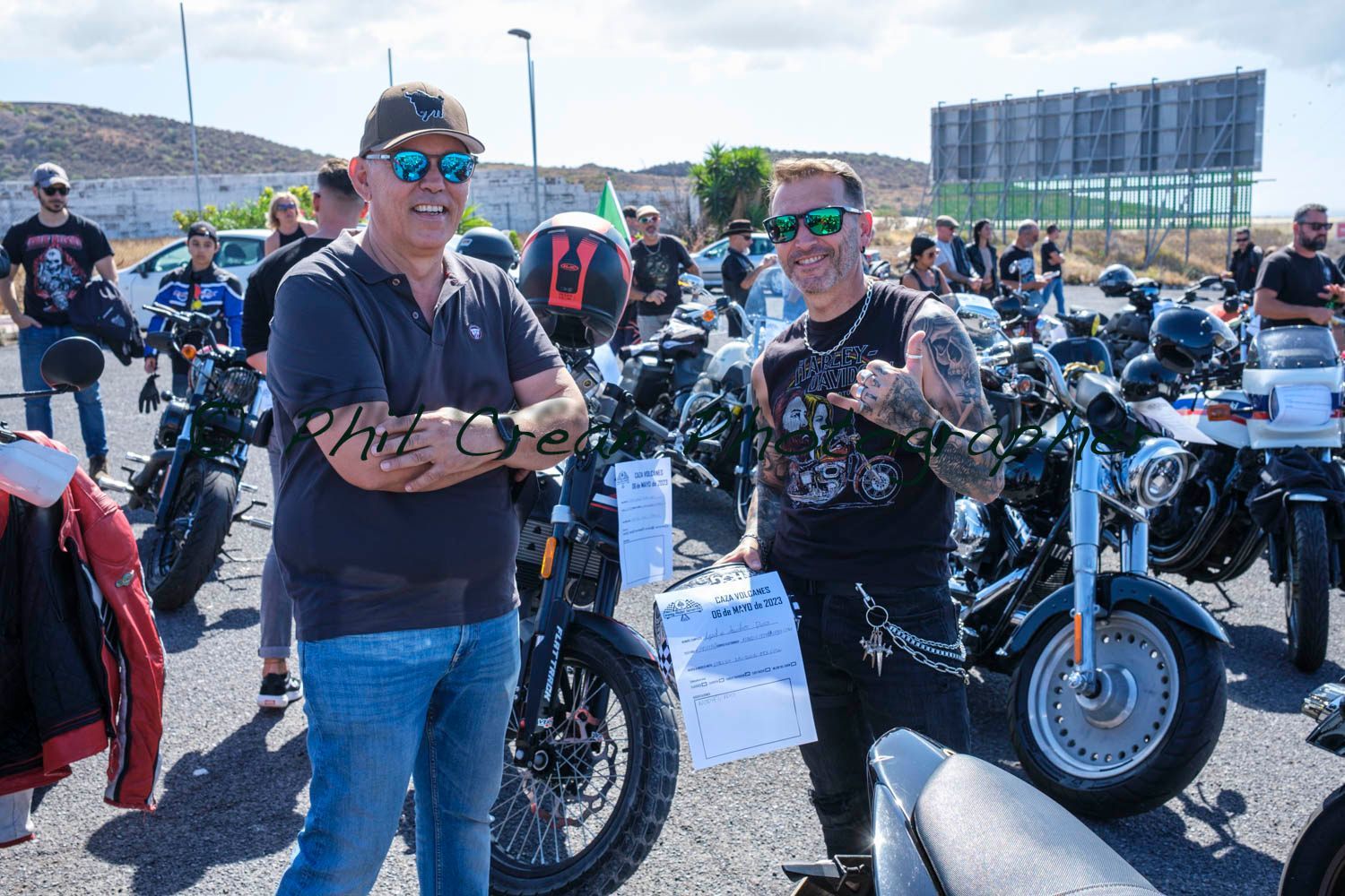 Two men are standing next to each other in front of a row of motorcycles.