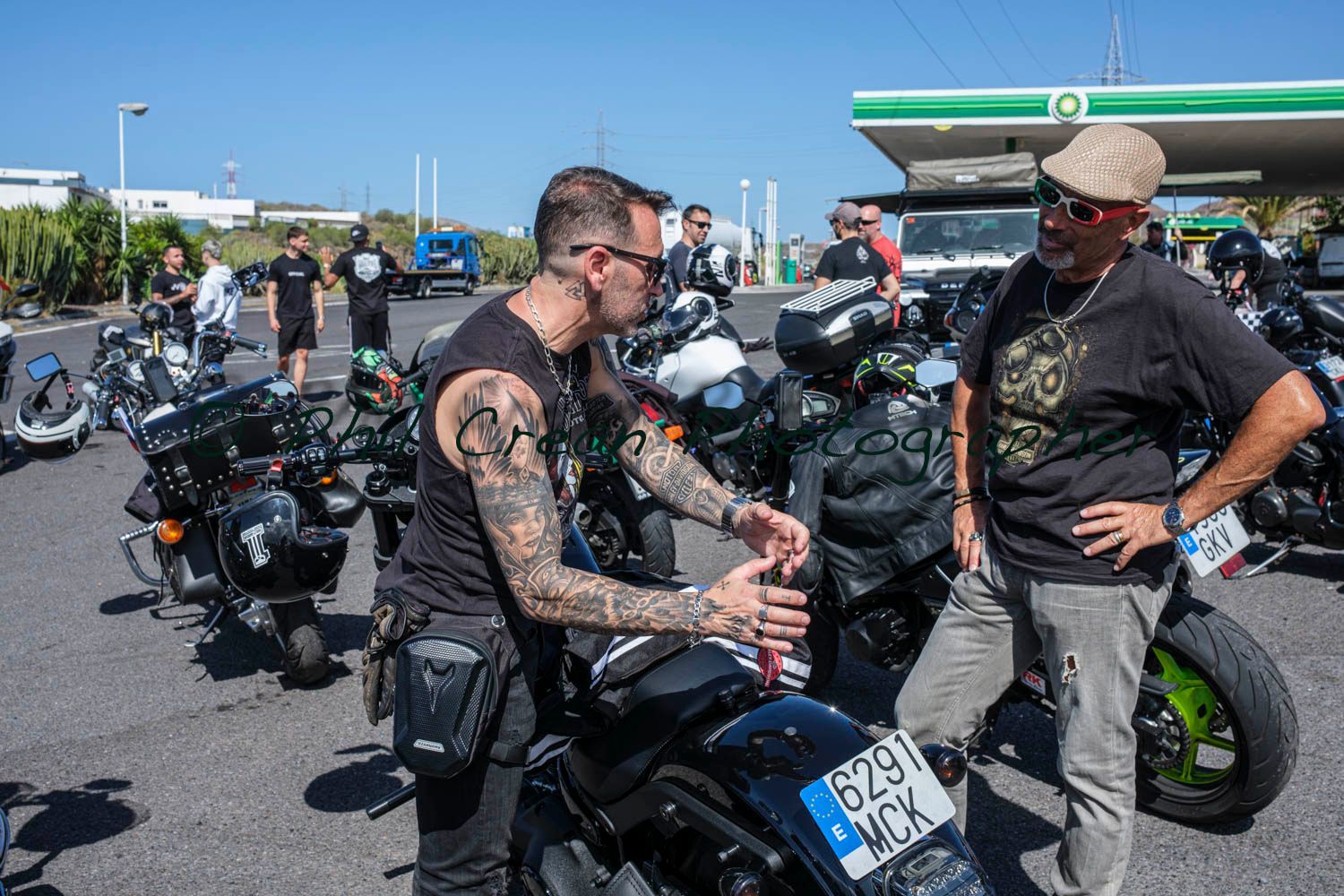 A group of men are standing around motorcycles at a gas station.