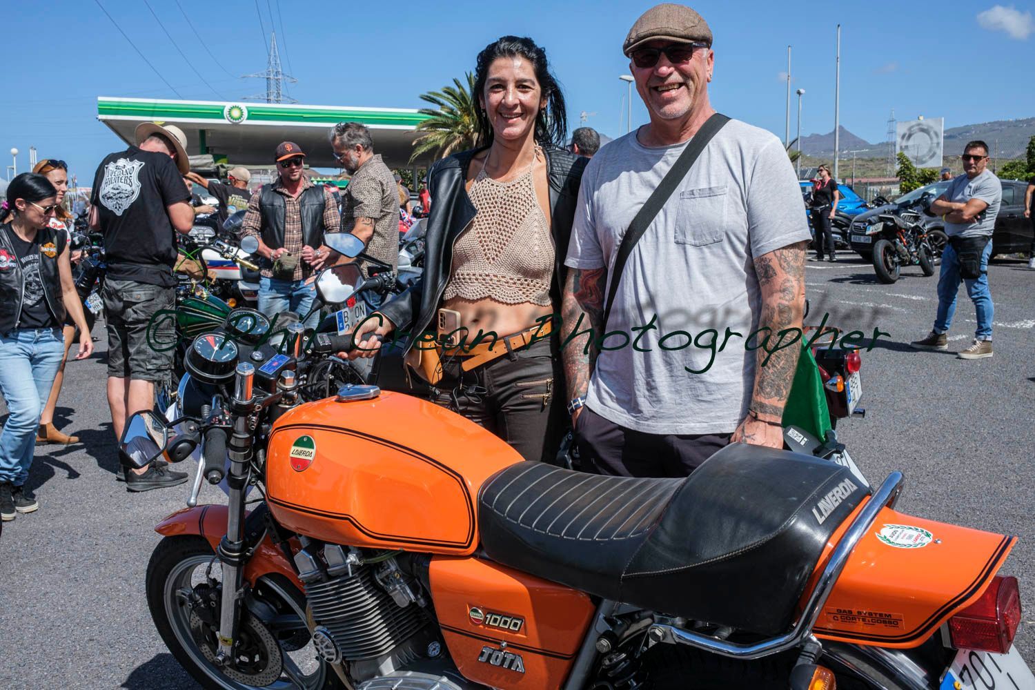 A man and a woman are standing next to an orange motorcycle.