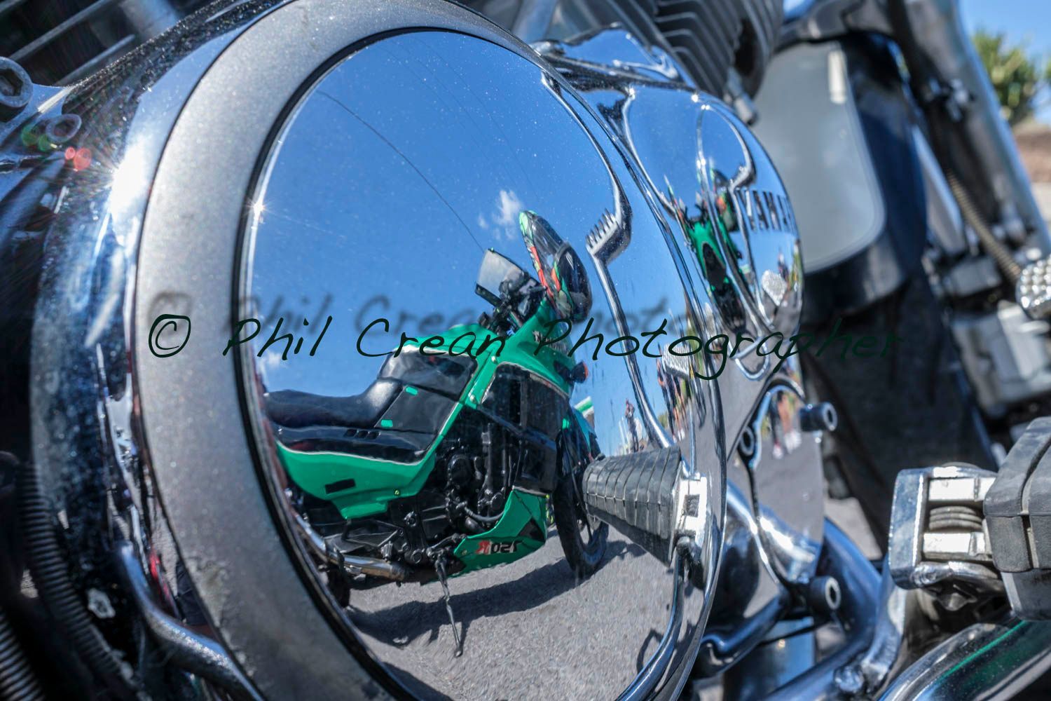 A green motorcycle is reflected in a chrome engine cover
